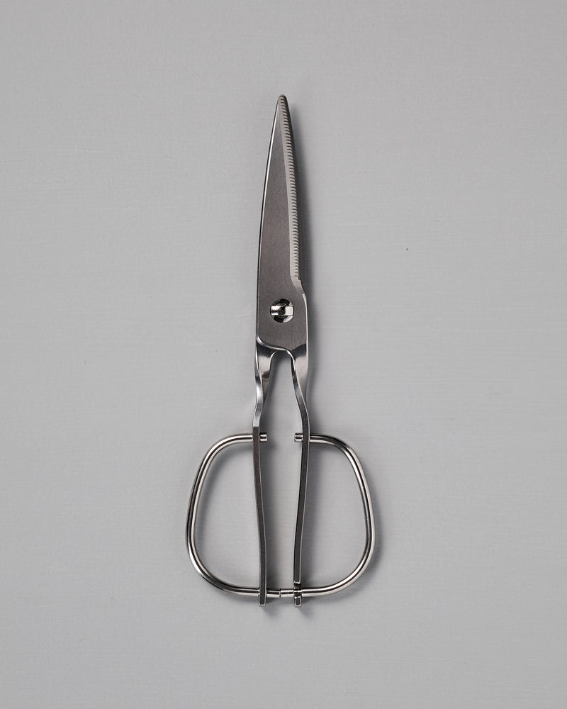 A pair of stainless steel kitchen shears with wide handles is placed on a plain gray surface.