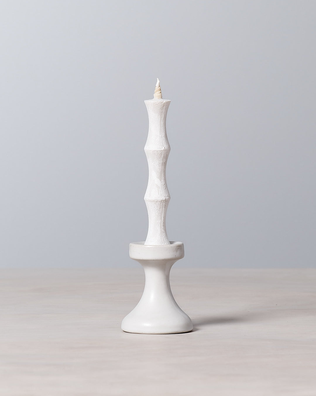 A FLUID – Stoneware Candle Holder by Takazawa is sitting on top of a stoneware table.