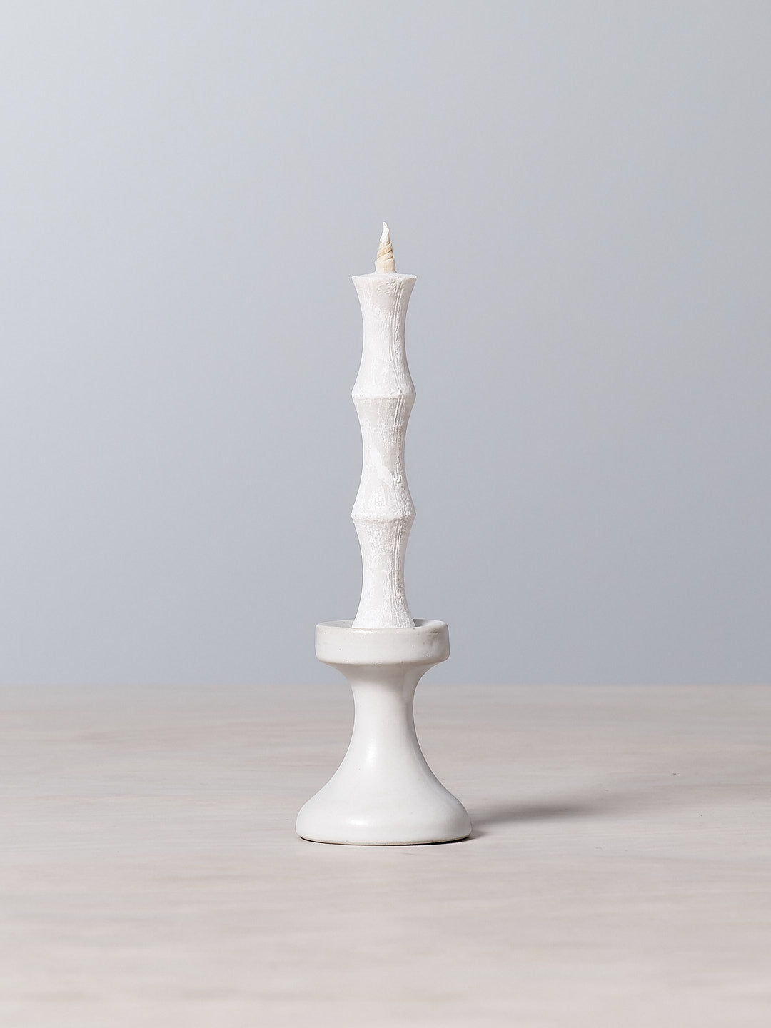A FLUID – Stoneware Candle Holder by Takazawa is sitting on top of a stoneware table.