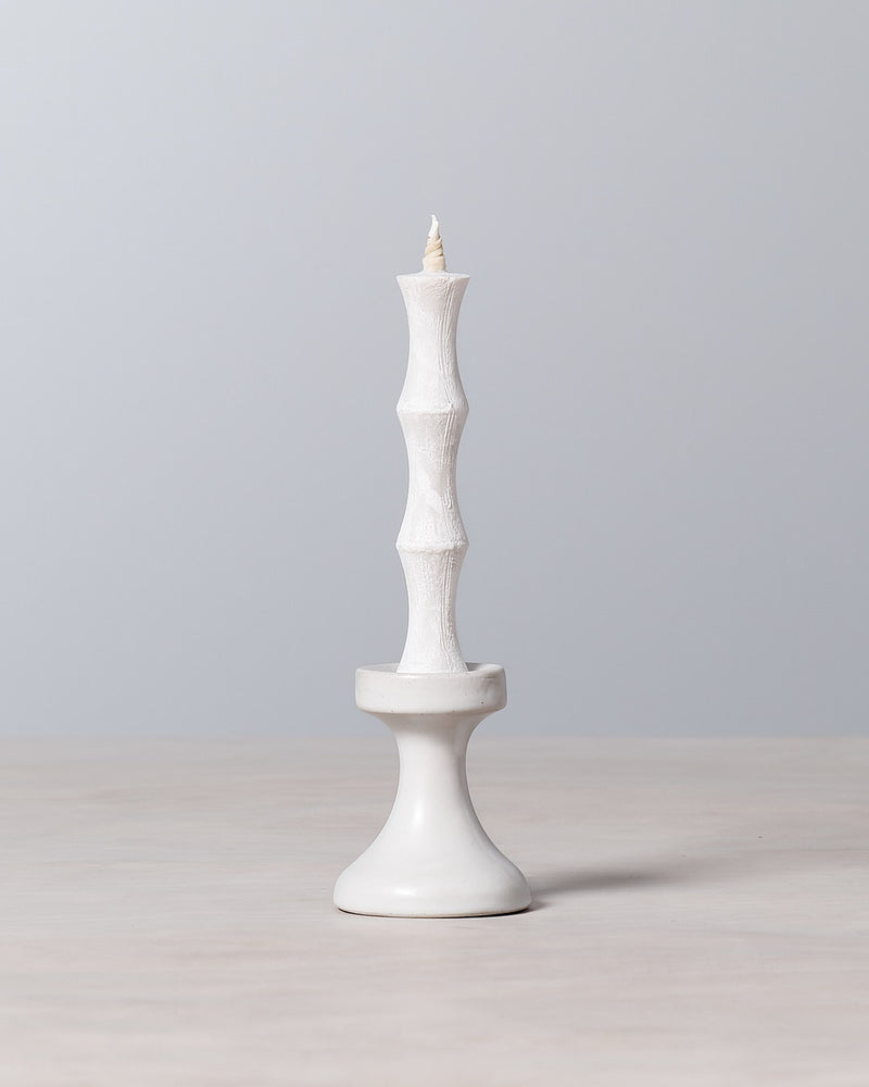 A FLUID – Stoneware Candle Holder by Takazawa is sitting on top of a stoneware table.