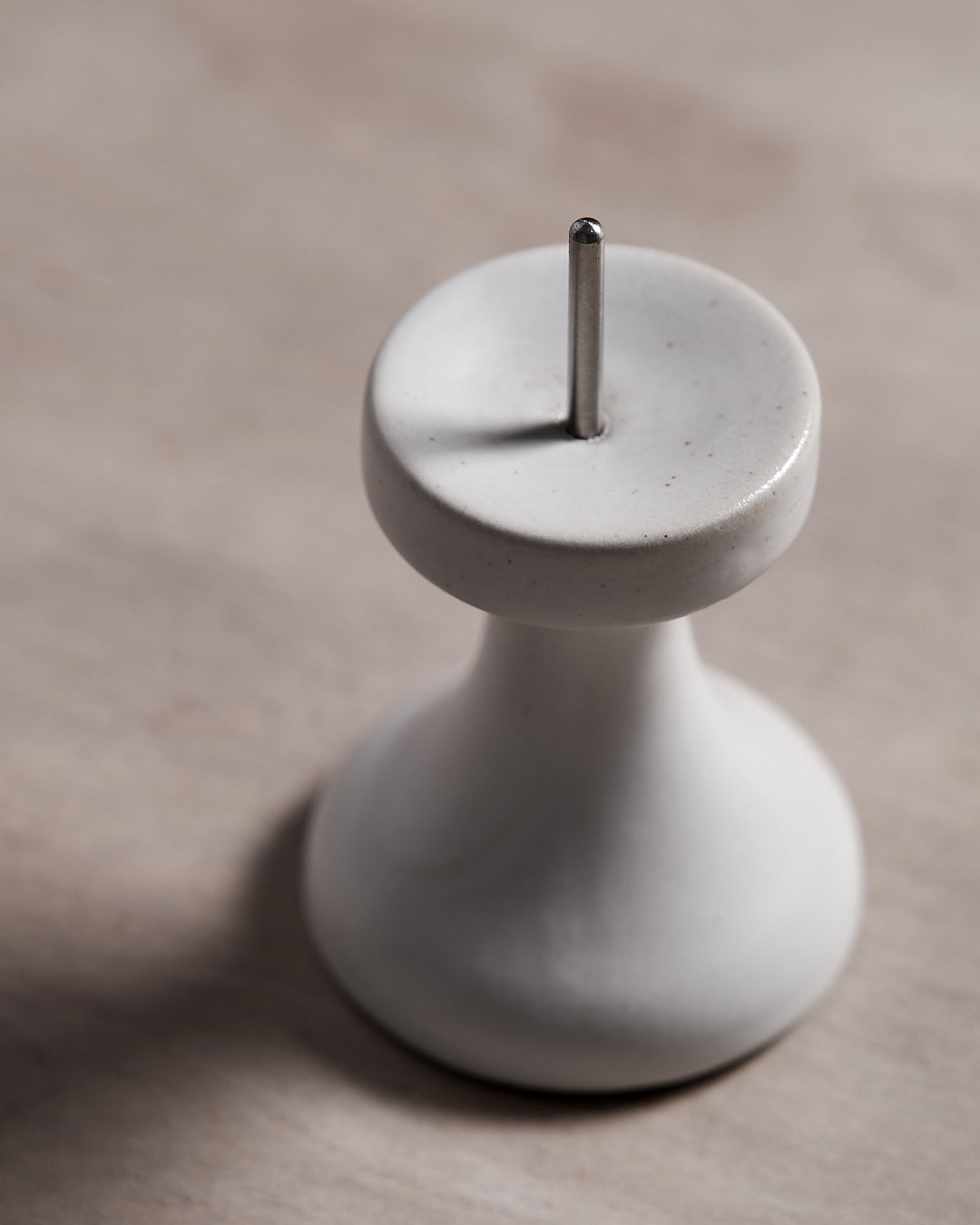 A small white FLUID – Stoneware Candle Holder by Takazawa on a wooden table.