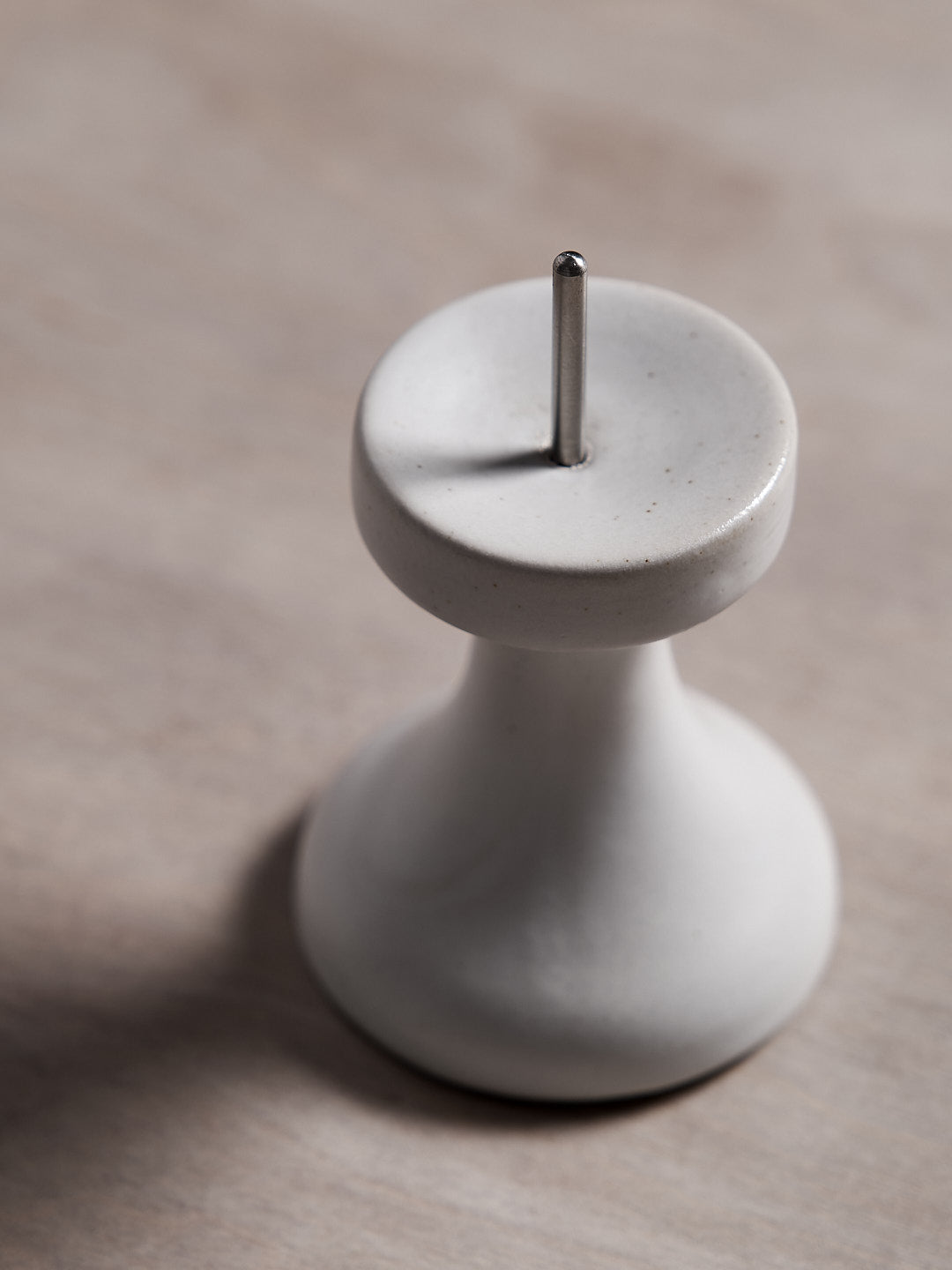 A small white FLUID – Stoneware Candle Holder by Takazawa on a wooden table.