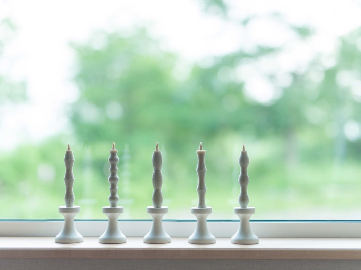 Five FLUID – Stoneware Candle Holders are lined up on a window sill, all made by Takazawa brand.