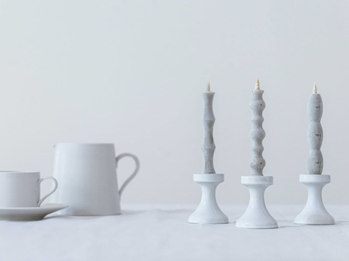 Three FLUID – Stoneware Candle Holders by Takazawa on a table next to a cup and saucer.