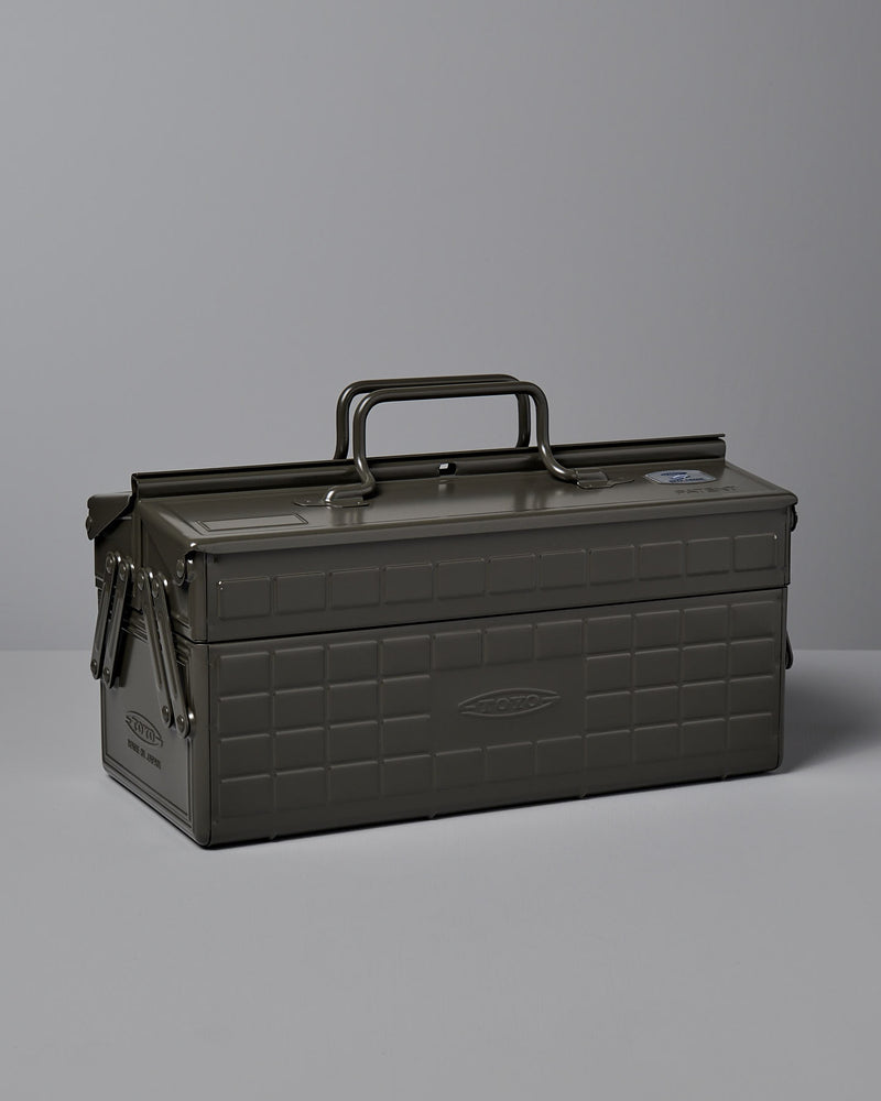 A moss green, powder-coated steel TOYO STEEL Cantilever Toolbox ST-350 with a rectangular shape, clasped lid, and a single handle on top, placed on a gray surface. Made in Osaka.