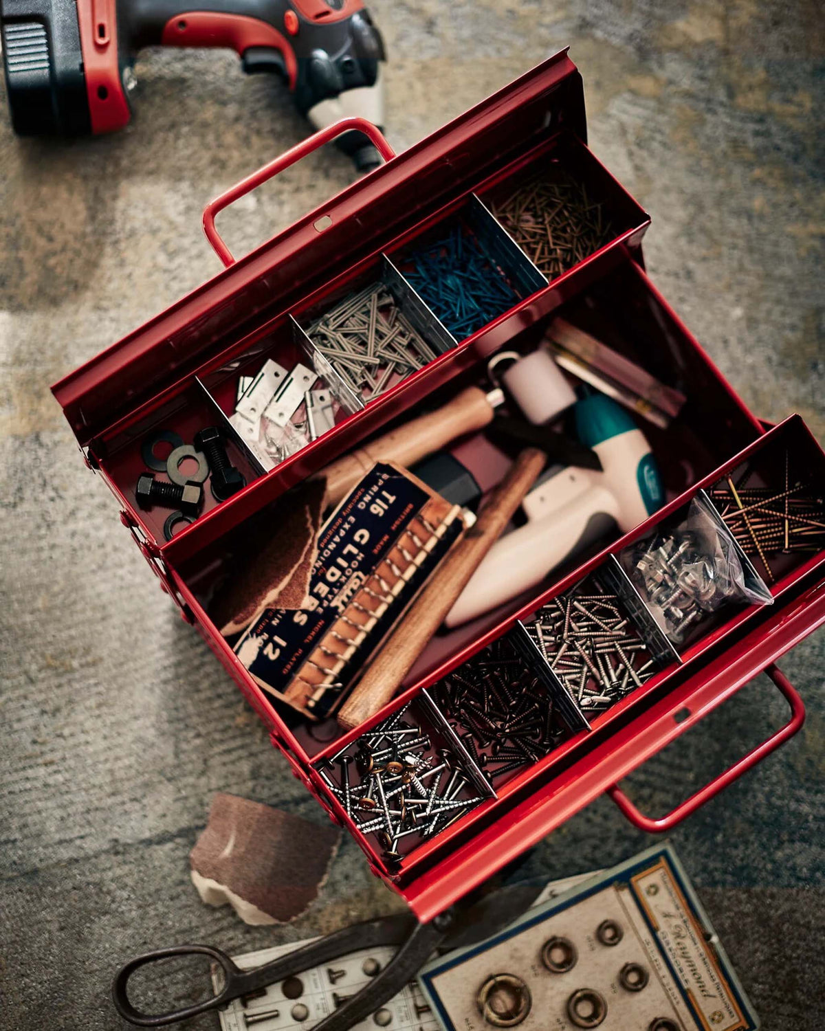Red metal tool box containing various hardware, screws, and small tools.