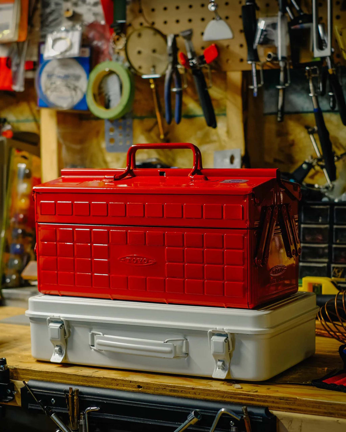 A red metal tool box stacked on top of a white metal tool box on a wooden workbench.