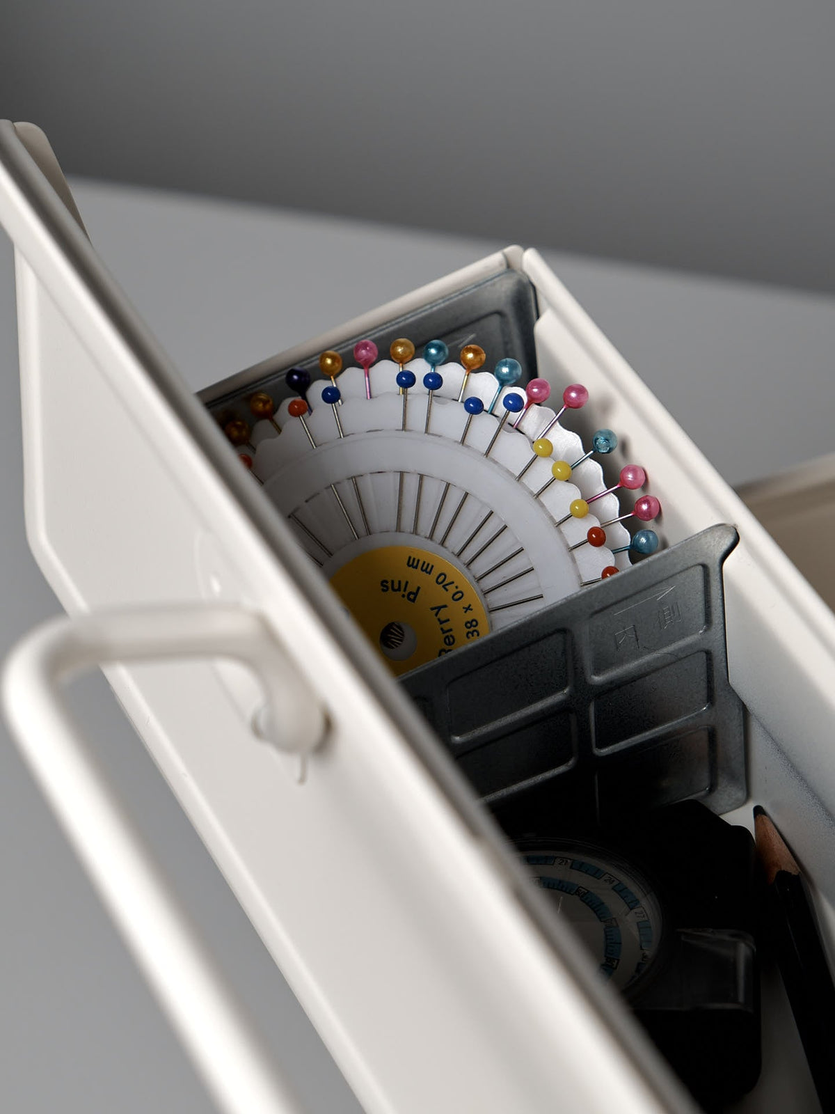 A close-up of a TOYO STEEL Cantilever Toolbox ST-350 – White made from powder-coated steel holds colored sewing pins arranged in a circular holder, with other small sewing supplies visible.