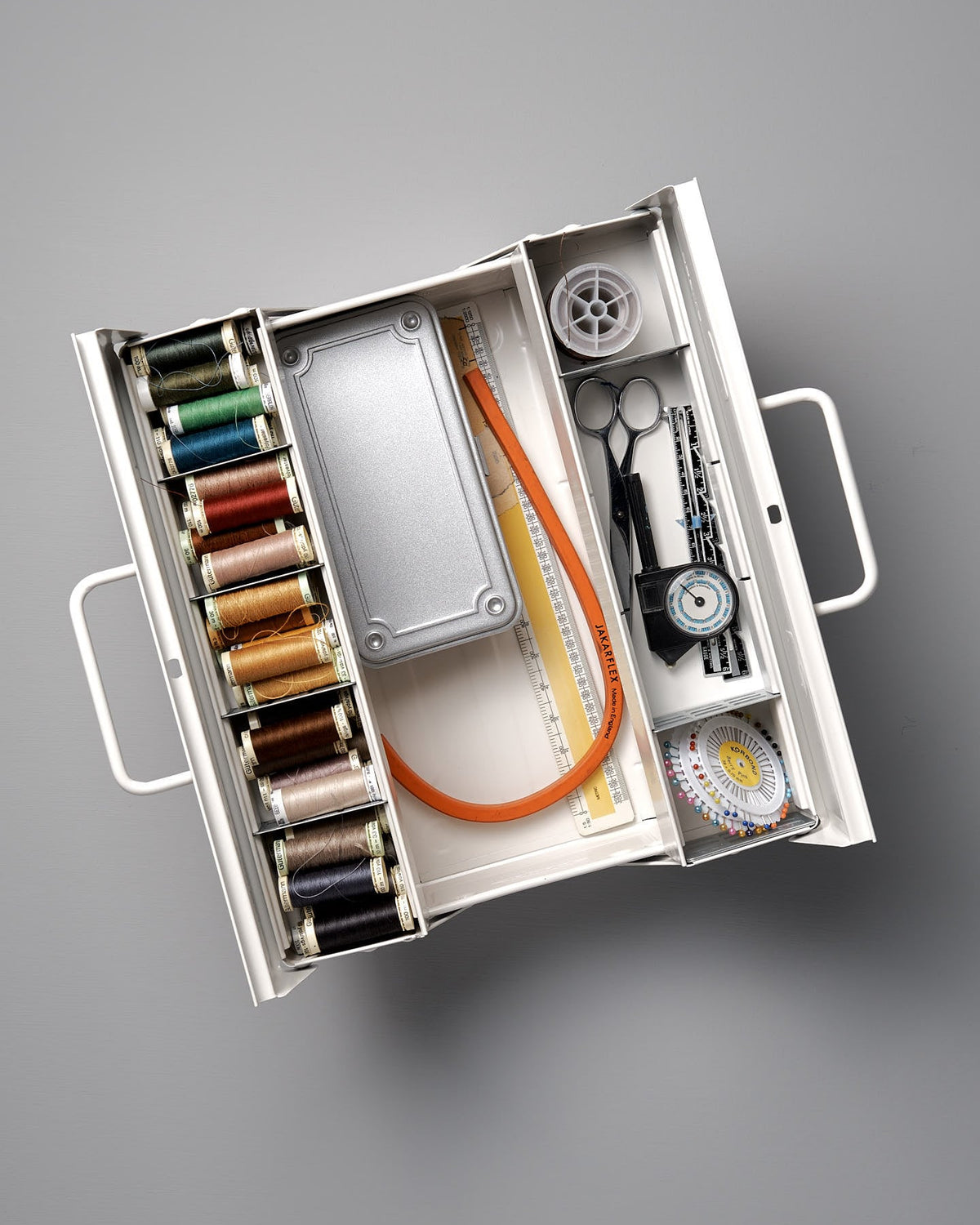 Open Cantilever Toolbox ST-350 – White by TOYO STEEL containing multiple spools of thread, a measuring tape, scissors, and various sewing tools neatly arranged within an iconic camber-top toolbox.