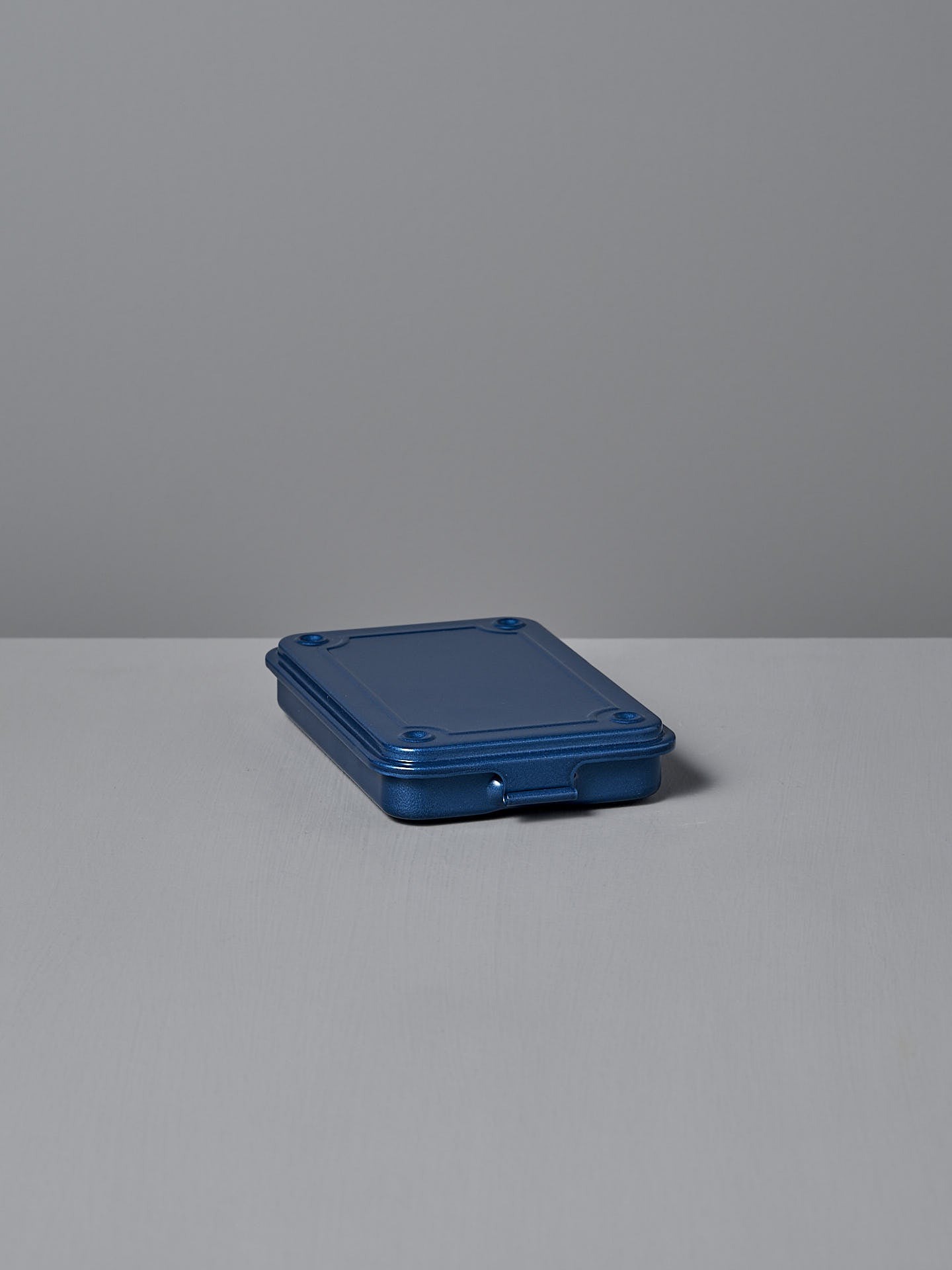 The Mini Steel Toolbox T-152 by TOYO STEEL, featuring a closed, rectangular design with rounded edges in blue, rests on a gray surface against a gray background. It's a sleek and practical storage solution that fits seamlessly into any space.
