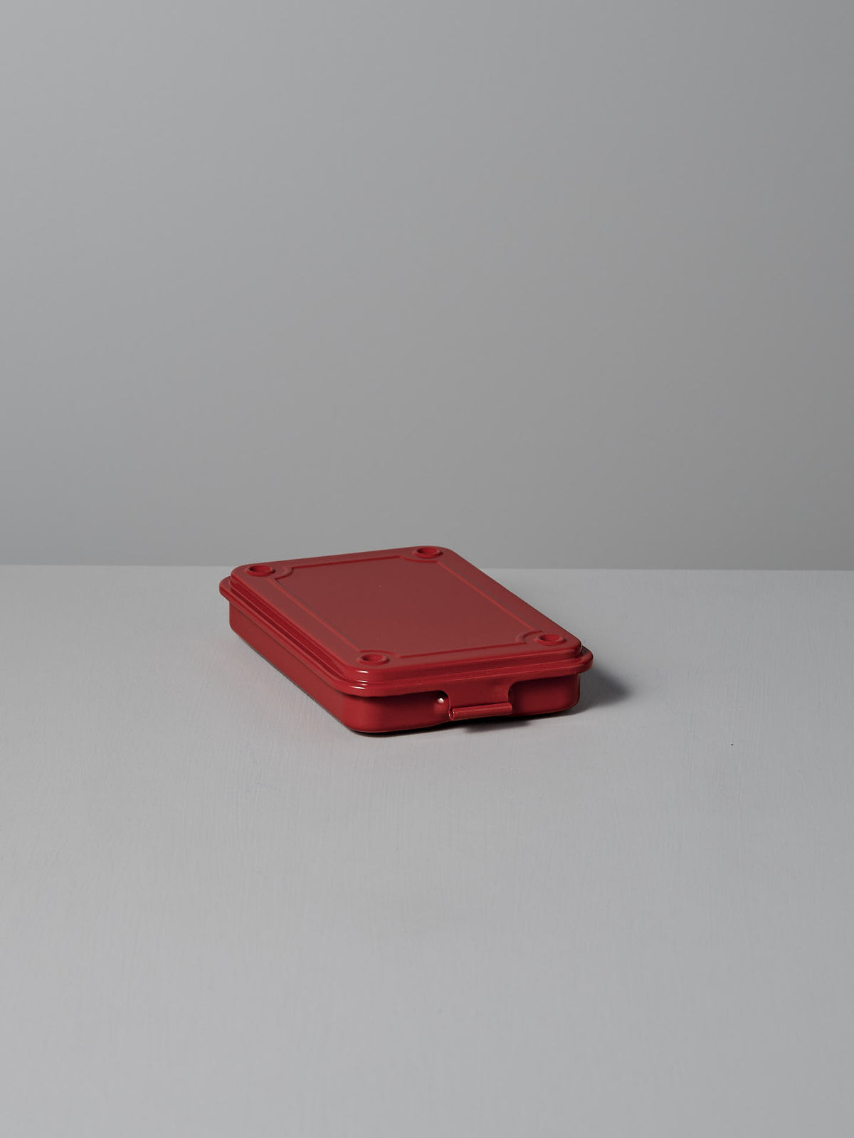 A rectangular Mini Steel Toolbox T-152 in red from TOYO STEEL, reminiscent of a versatile storage solution, sits on a flat surface against a gray background.