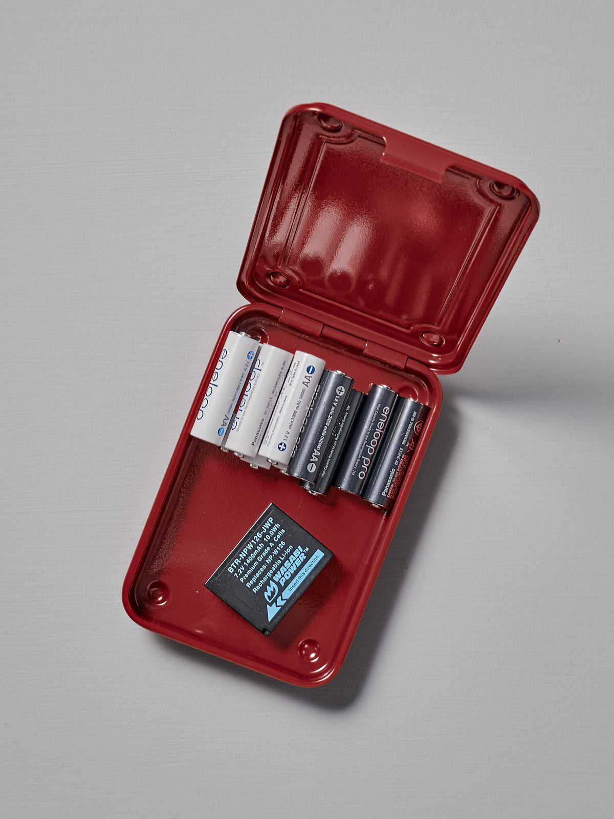 A Mini Steel Toolbox T-152 – Red by TOYO STEEL stores various AA and AAA batteries and includes a small instruction card inside.