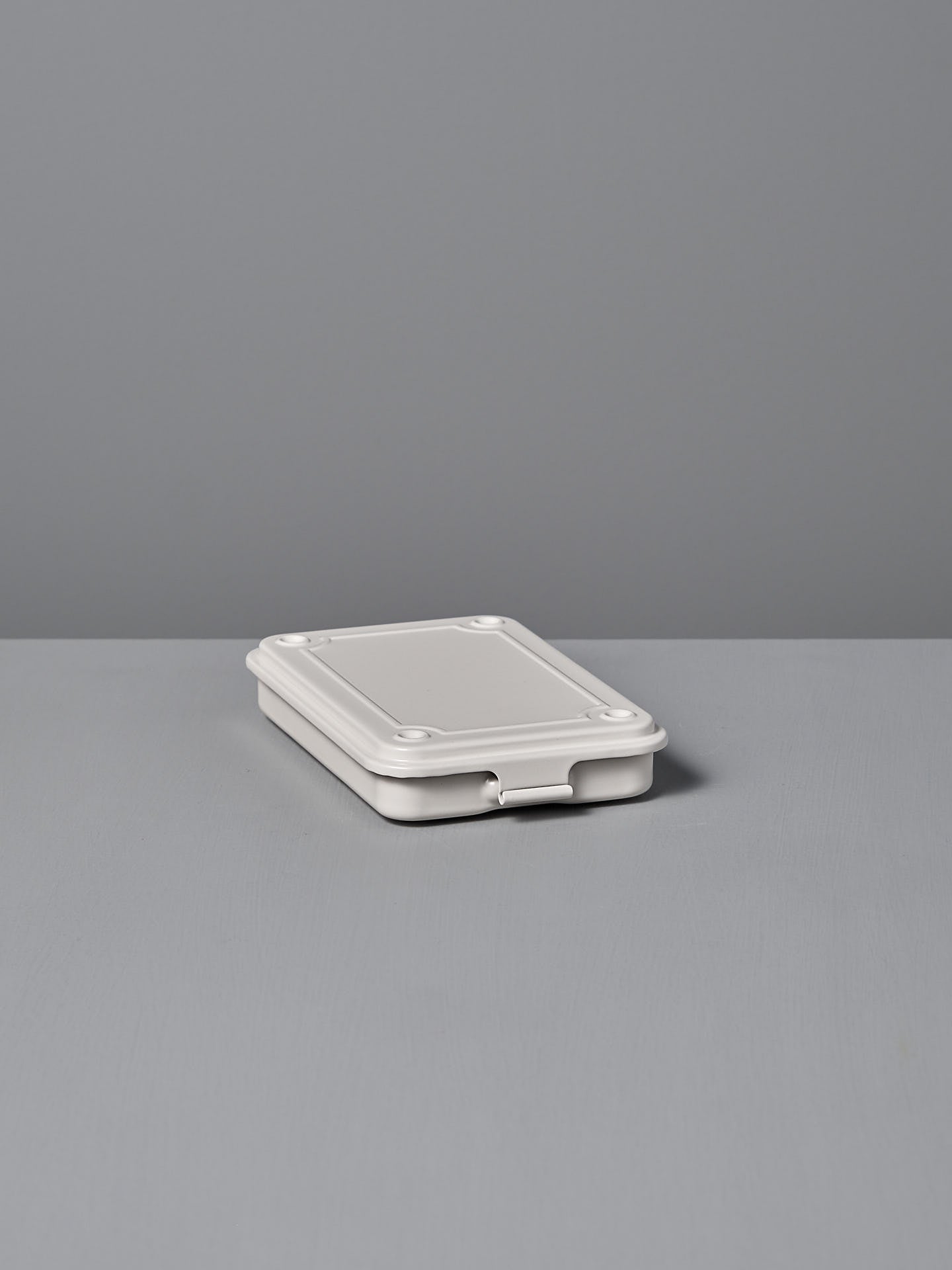 The Mini Steel Toolbox T-152 – White by TOYO STEEL, a closed powder-coated steel container, sits elegantly on a gray surface against a light gray background.