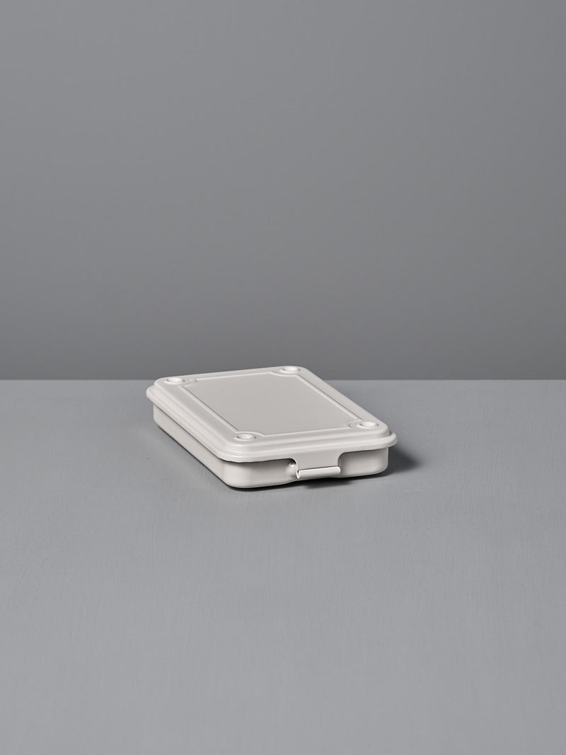 The Mini Steel Toolbox T-152 – White by TOYO STEEL, a closed powder-coated steel container, sits elegantly on a gray surface against a light gray background.