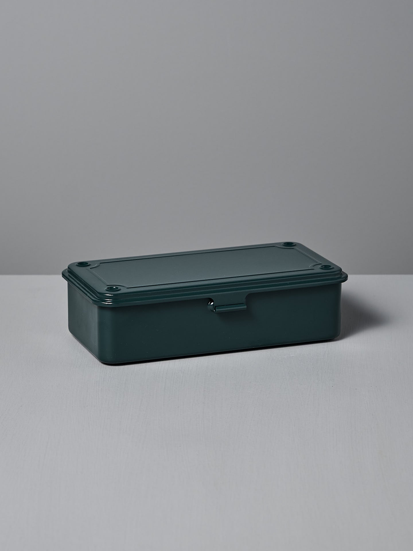 The Mini Steel Toolbox T-190 by TOYO STEEL features an antique green finish, crafted from powder-coated steel with a closed lid, and rests elegantly on a gray surface.