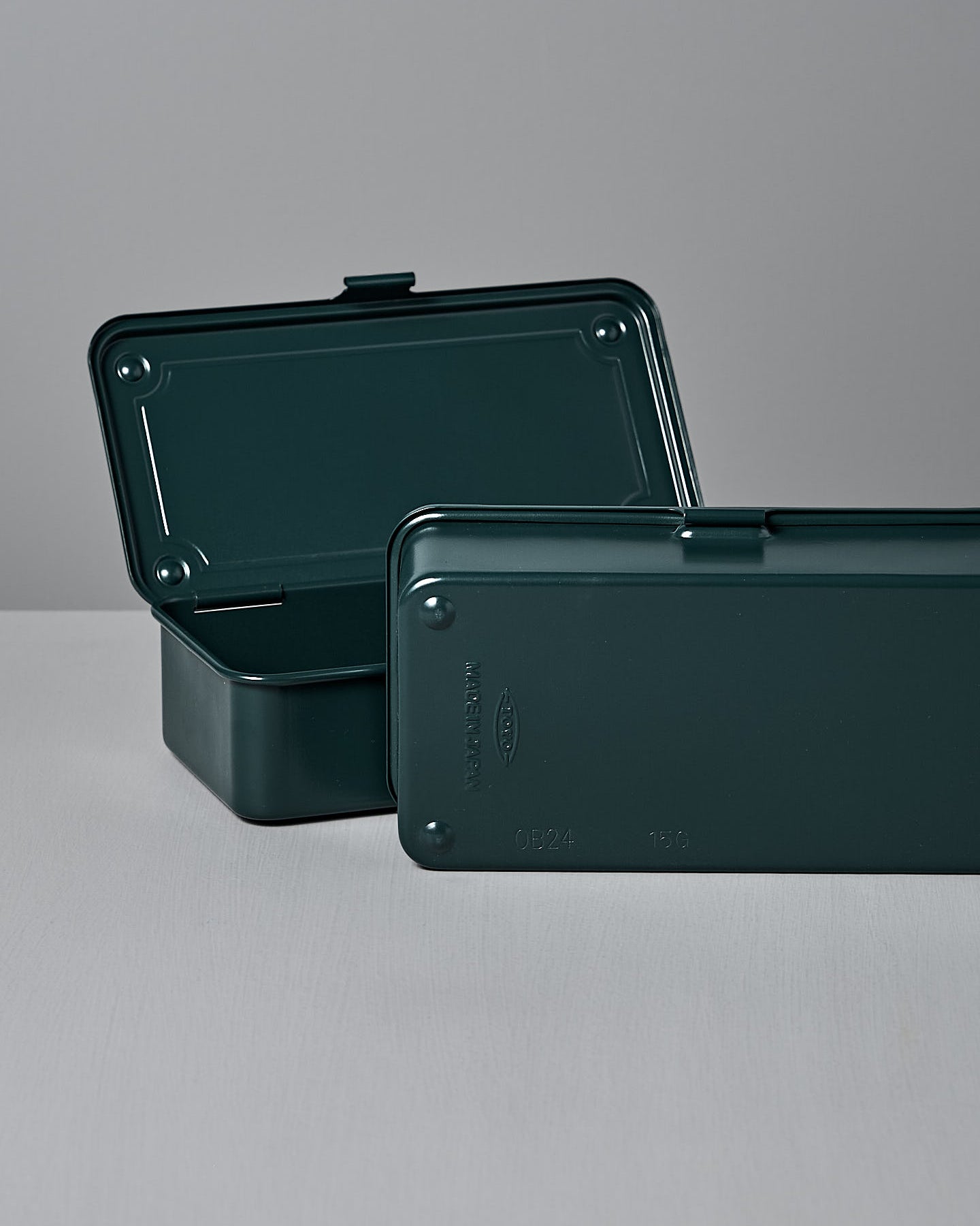 The Mini Steel Toolbox T-190 by TOYO STEEL features an antique green finish, crafted from powder-coated steel with a closed lid, and rests elegantly on a gray surface.