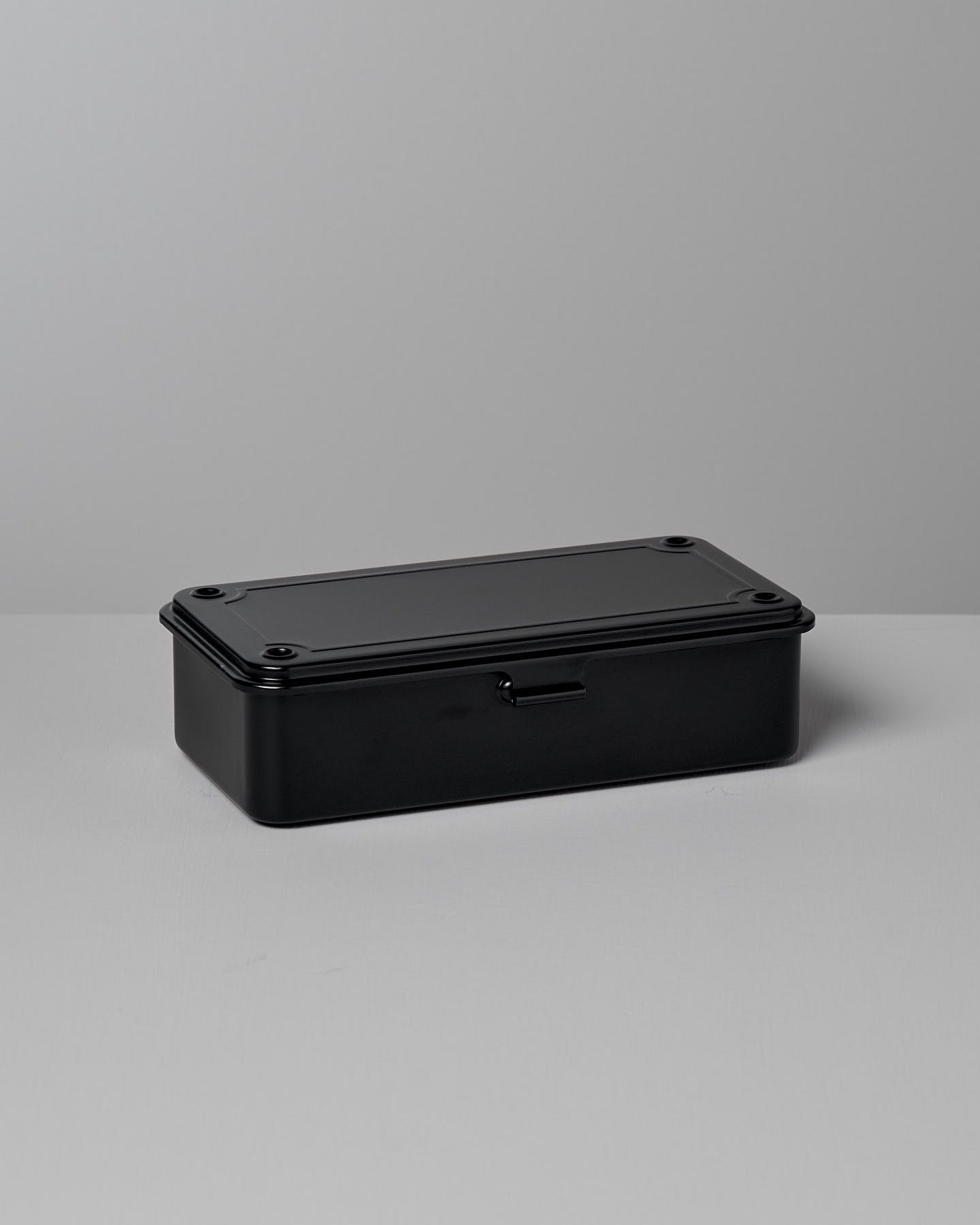 A TOYO STEEL Mini Steel Toolbox T-190 – Black, with rounded edges, sits on a light gray surface against a matching background, showcasing its strong design as an elegant storage solution.