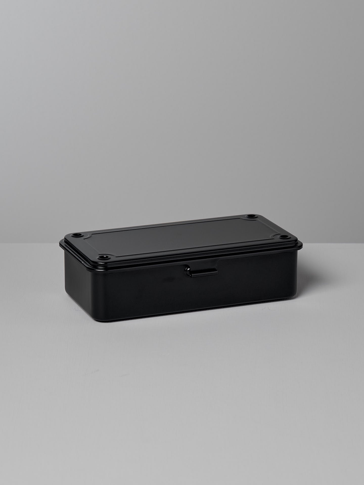 A TOYO STEEL Mini Steel Toolbox T-190 – Black, with rounded edges, sits on a light gray surface against a matching background, showcasing its strong design as an elegant storage solution.