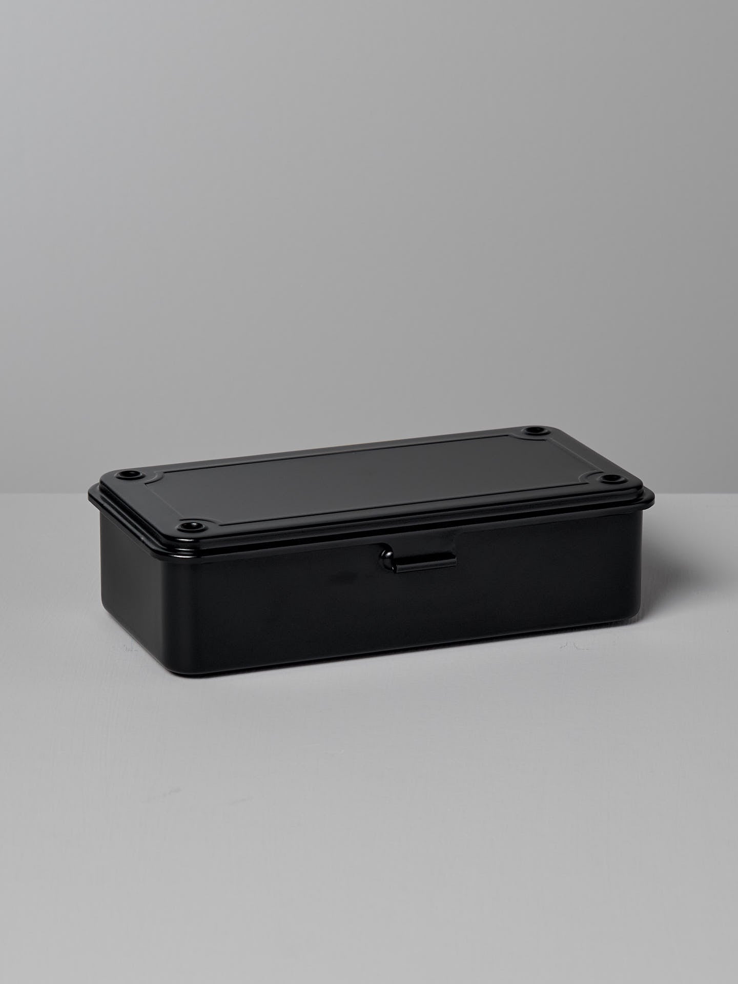 A TOYO STEEL Mini Steel Toolbox T-190 – Black, with rounded edges, sits on a light gray surface against a matching background, showcasing its strong design as an elegant storage solution.