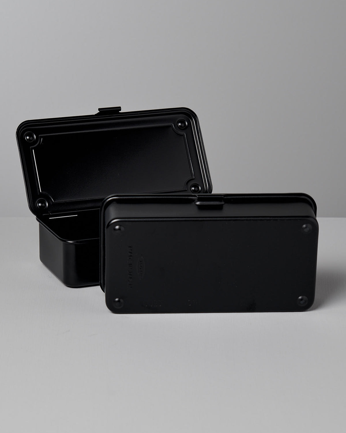 Two black Mini Steel Toolbox T-190 – Black storage boxes by TOYO STEEL are displayed, one with the lid open showing the interior and the other with the lid closed. The surfaces are smooth with rounded edges and visible rivets, showcasing a strong design as an effective storage solution.