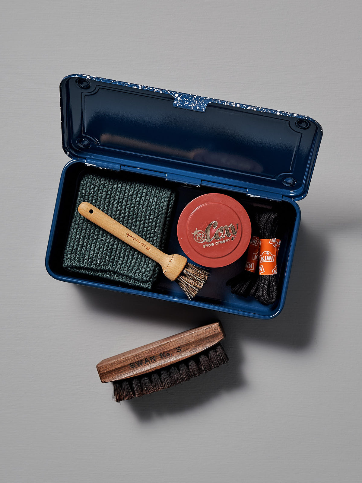 The Mini Steel Toolbox T-190 – Japanese Indigo by TOYO STEEL comes in a sleek, powder-coated steel storage box and includes shoe cream, a small brush, cloth, larger brush, laces, and polish. It is displayed open on a gray surface for easy access and organization.