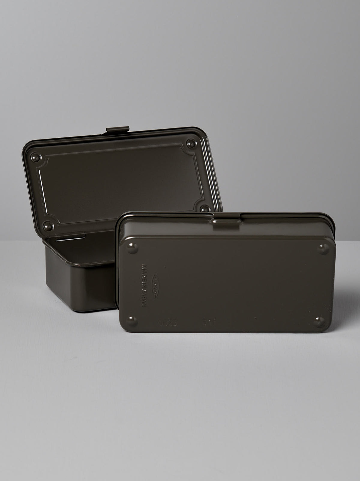 Two rectangular dark-colored steel storage boxes with lids, made in Japan. One Mini Steel Toolbox T-190 – Moss Green by TOYO STEEL is open and the other is closed, placed on a gray surface with a plain gray background. Their versatile design makes them perfect for any space.