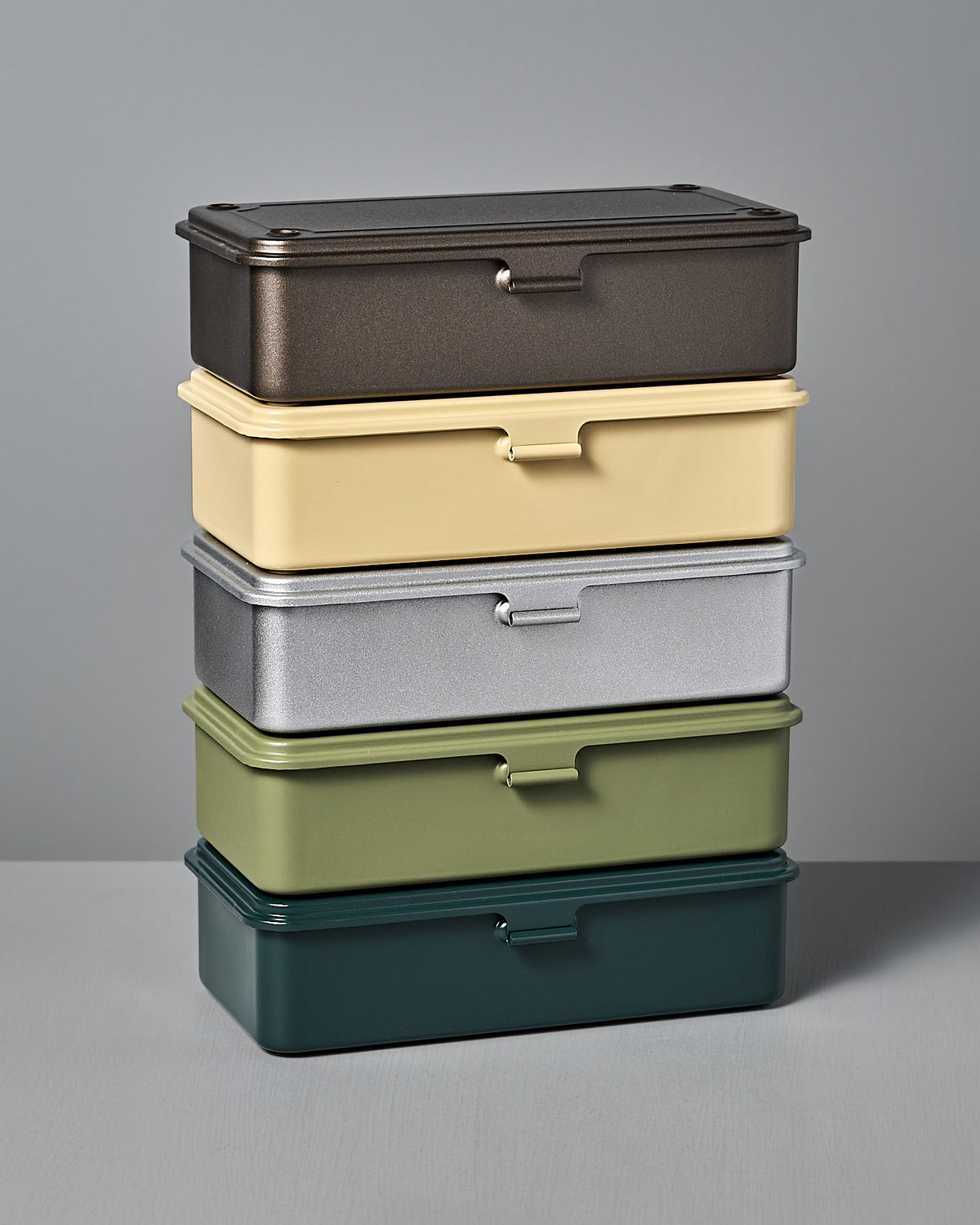 A set of five stackable TOYO STEEL Mini Steel Toolbox T-190s in titanium finish, featuring various colors like dark brown, beige, silver, green, and dark green on a neutral gray backdrop.