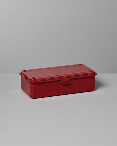 A Mini Steel Toolbox T-190 in red by TOYO STEEL, featuring a seamless rectangular design and a flat lid, sits on a light gray surface.
