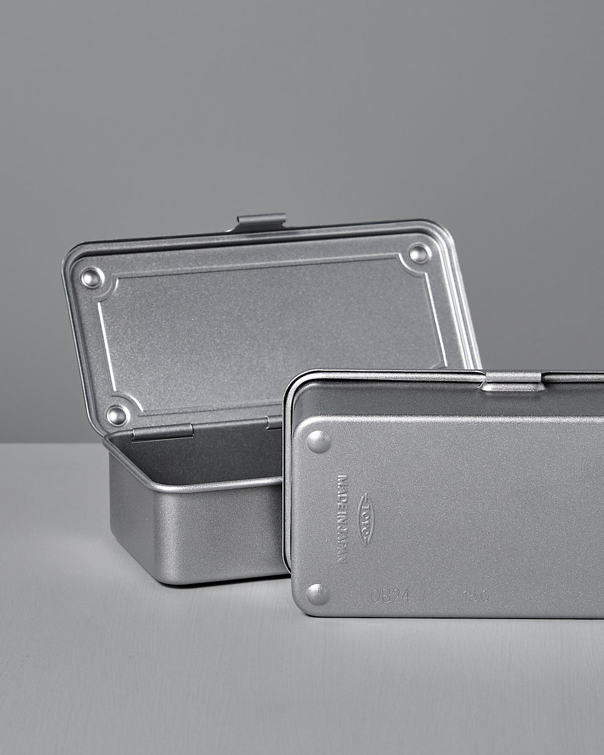 Two stackable Mini Steel Toolbox T-190 - Silver by TOYO STEEL—one open, one partially closed—rest elegantly on a light gray surface against a gray background.