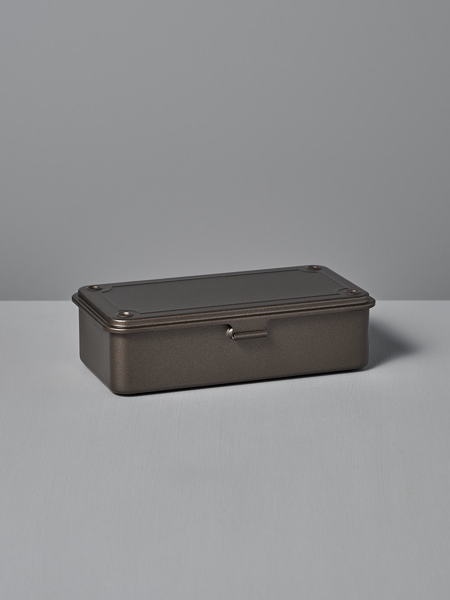 The Mini Steel Toolbox T-190 – Titanium by TOYO STEEL, a rectangular powder-coated tin box with a dark finish, hinged lid, and rivet details, is positioned on a flat surface against a plain background.
