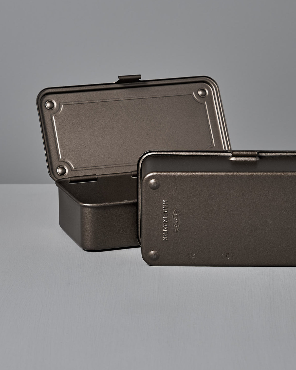 Two Mini Steel Toolboxes T-190 by TOYO STEEL, in titanium, rest on a light gray surface. One stands open to reveal its powder-coated steel interior as a versatile storage solution, while the other lies flat and closed, ready for use.