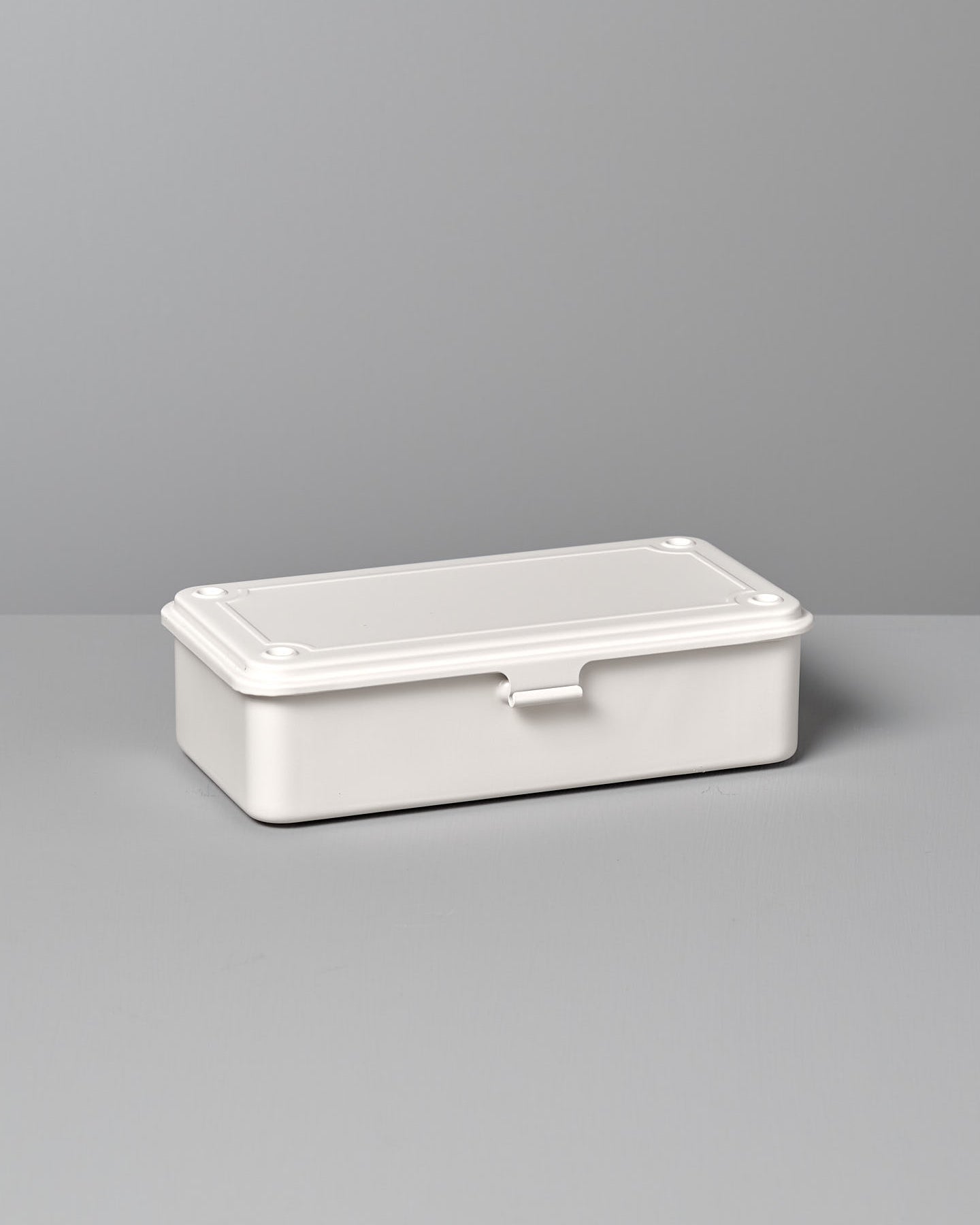 A Mini Steel Toolbox T-190 – White from TOYO STEEL with a closed lid, placed on a gray surface against a gray background.