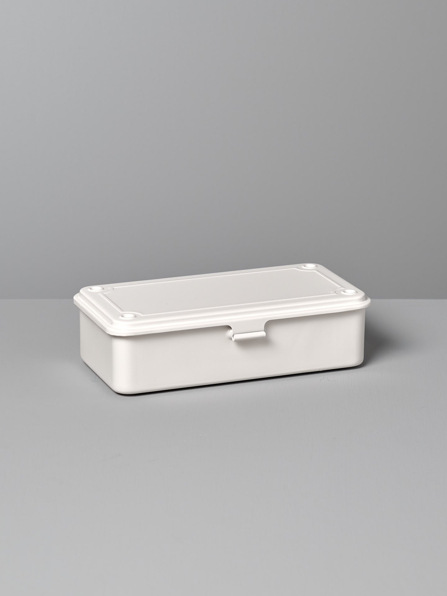 A Mini Steel Toolbox T-190 – White from TOYO STEEL with a closed lid, placed on a gray surface against a gray background.