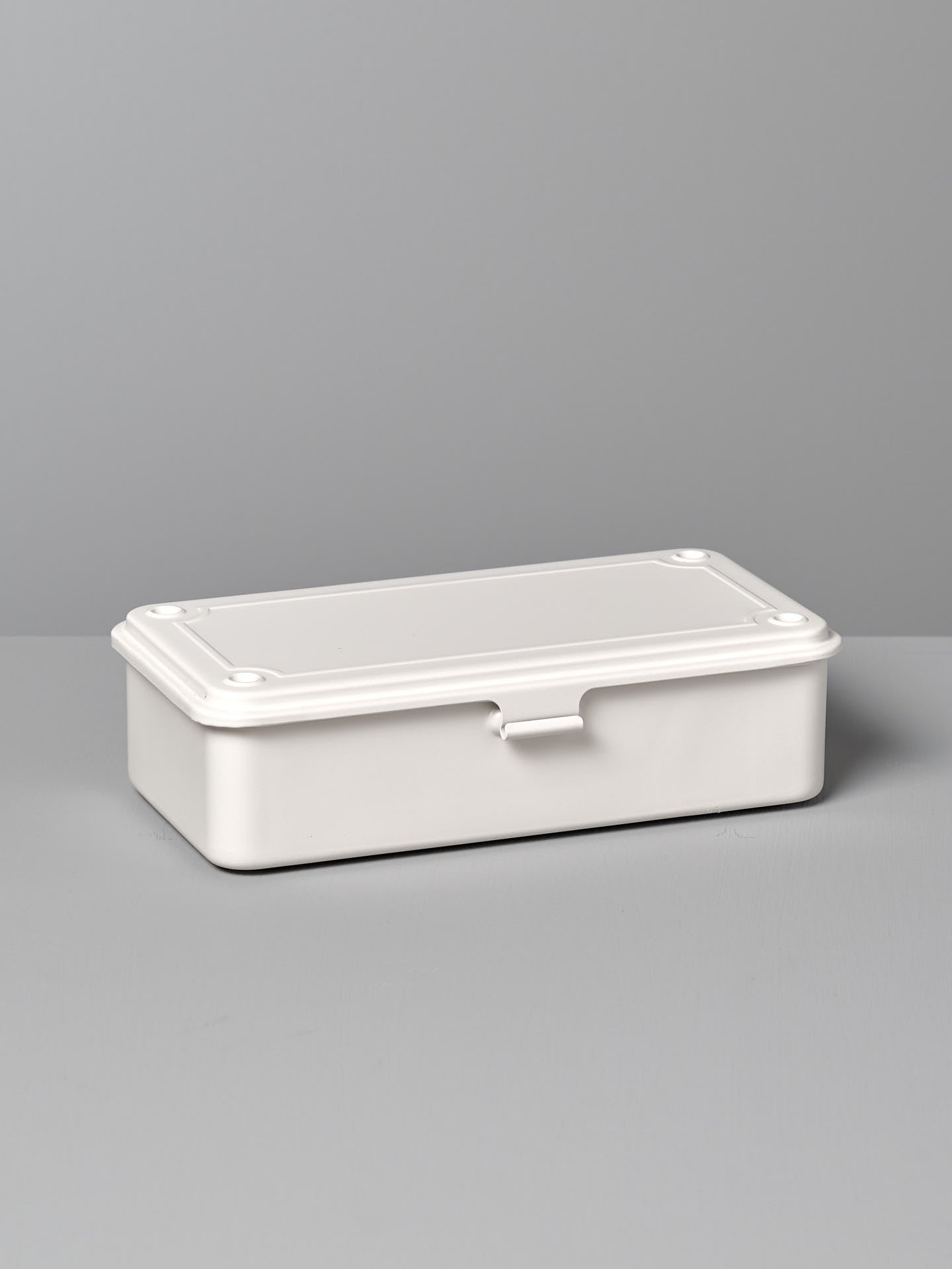 A Mini Steel Toolbox T-190 – White from TOYO STEEL with a closed lid, placed on a gray surface against a gray background.