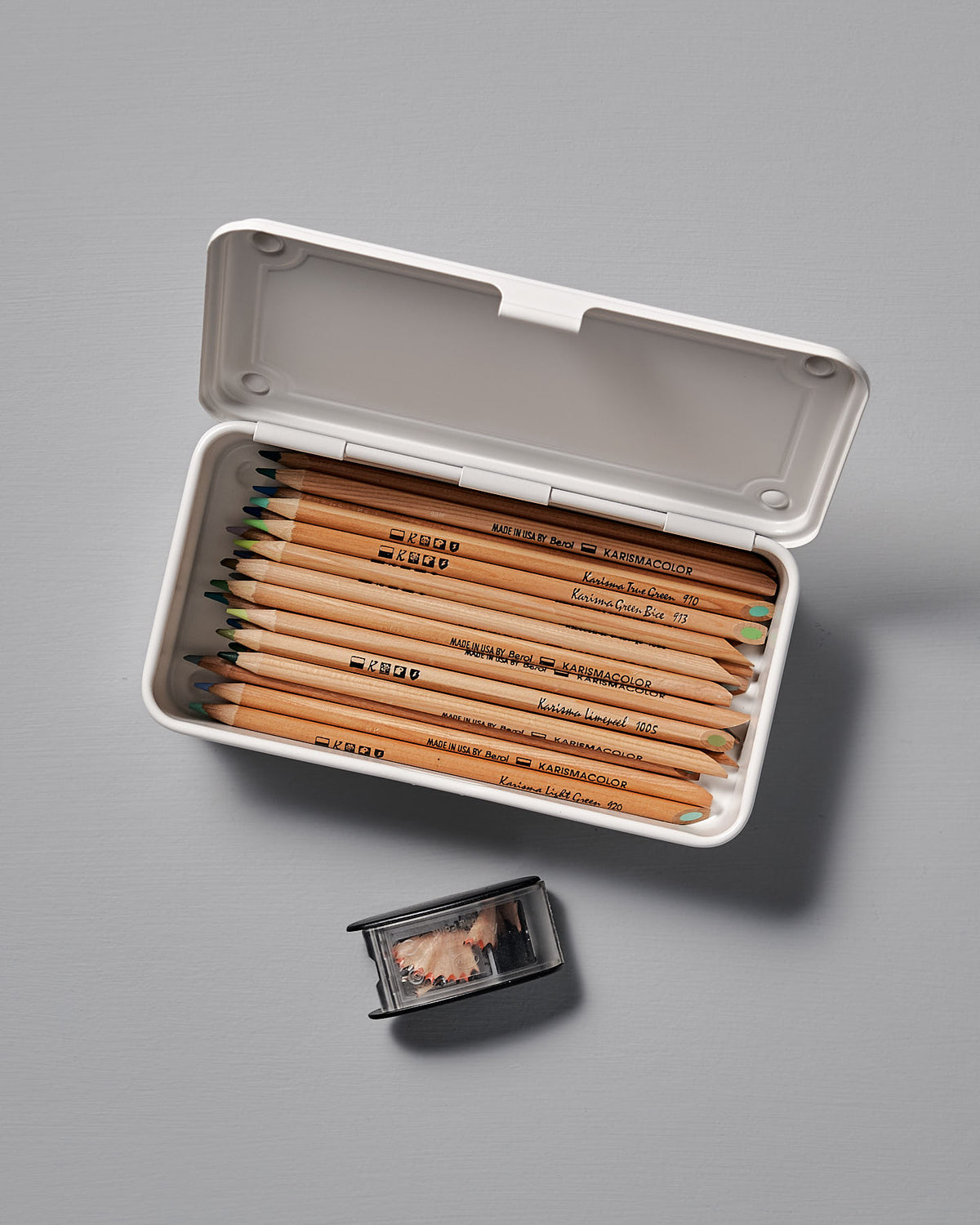 The Mini Steel Toolbox T-190 in white by TOYO STEEL features an open case with wooden colored pencils and a small pencil sharpener containing shavings on a gray surface, all neatly arranged in a sleek, stackable design.