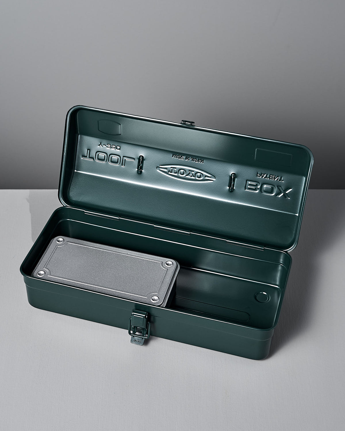 The Camber-Top Toolbox Y-350 by TOYO STEEL, in Antique Green, crafted from powder-coated steel, is open on a gray surface. Its small rectangular metal container inside exudes elegance reminiscent of the Good Design Award winners from 2009.