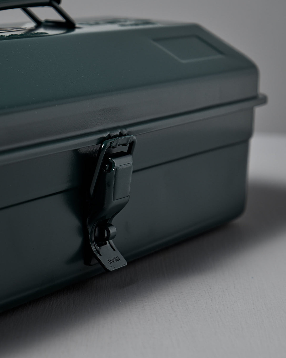 The Camber-Top Toolbox Y-350 in Antique Green by TOYO STEEL, made of powder-coated steel and featuring a secure latch, rests elegantly on a light surface.
