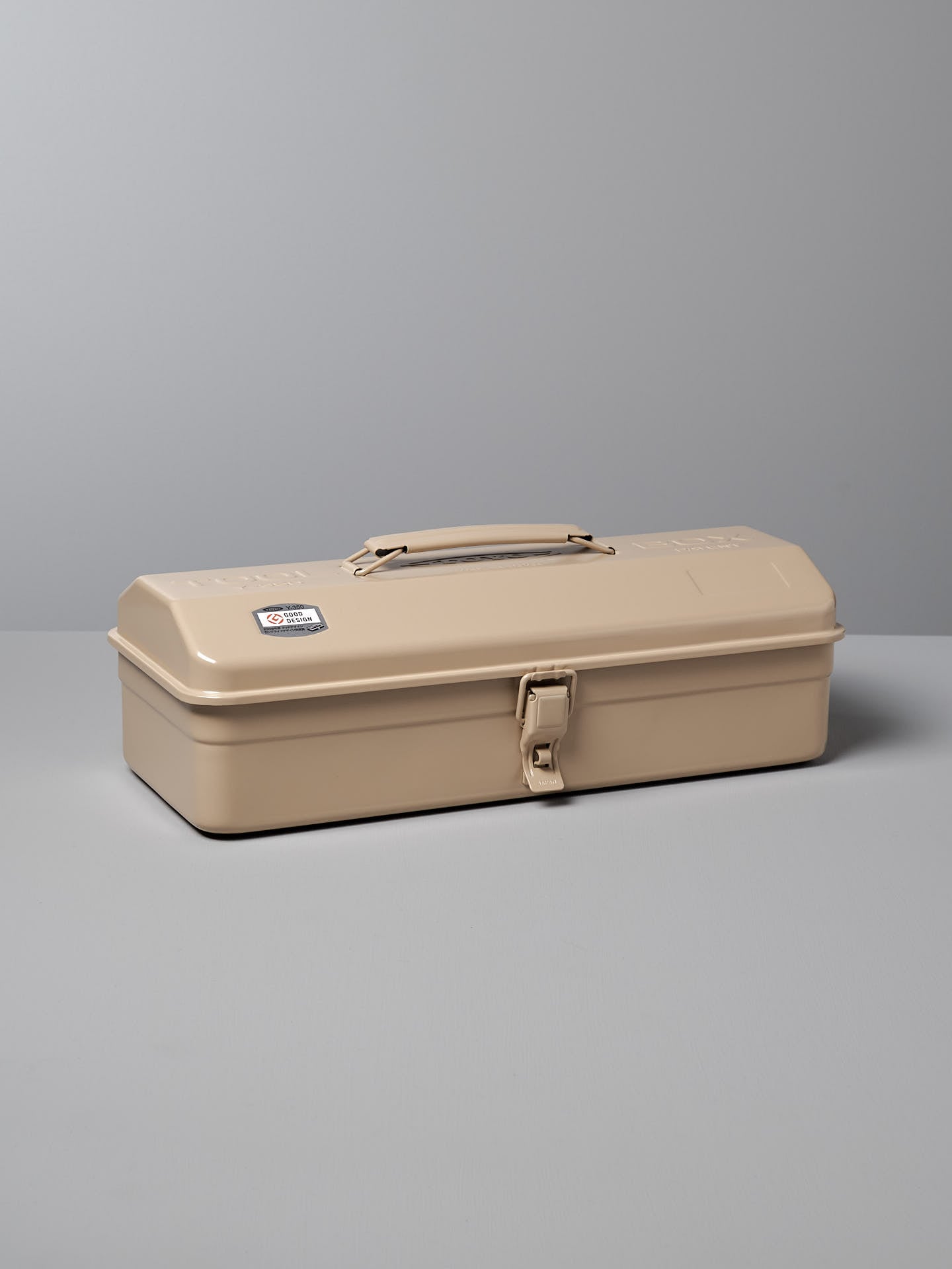 A versatile storage solution, the Camber-Top Toolbox Y-350 – Beige by TOYO STEEL, made in Japan, features a sturdy latch and a practical handle on top. It's elegantly placed on a grey surface against a grey background.