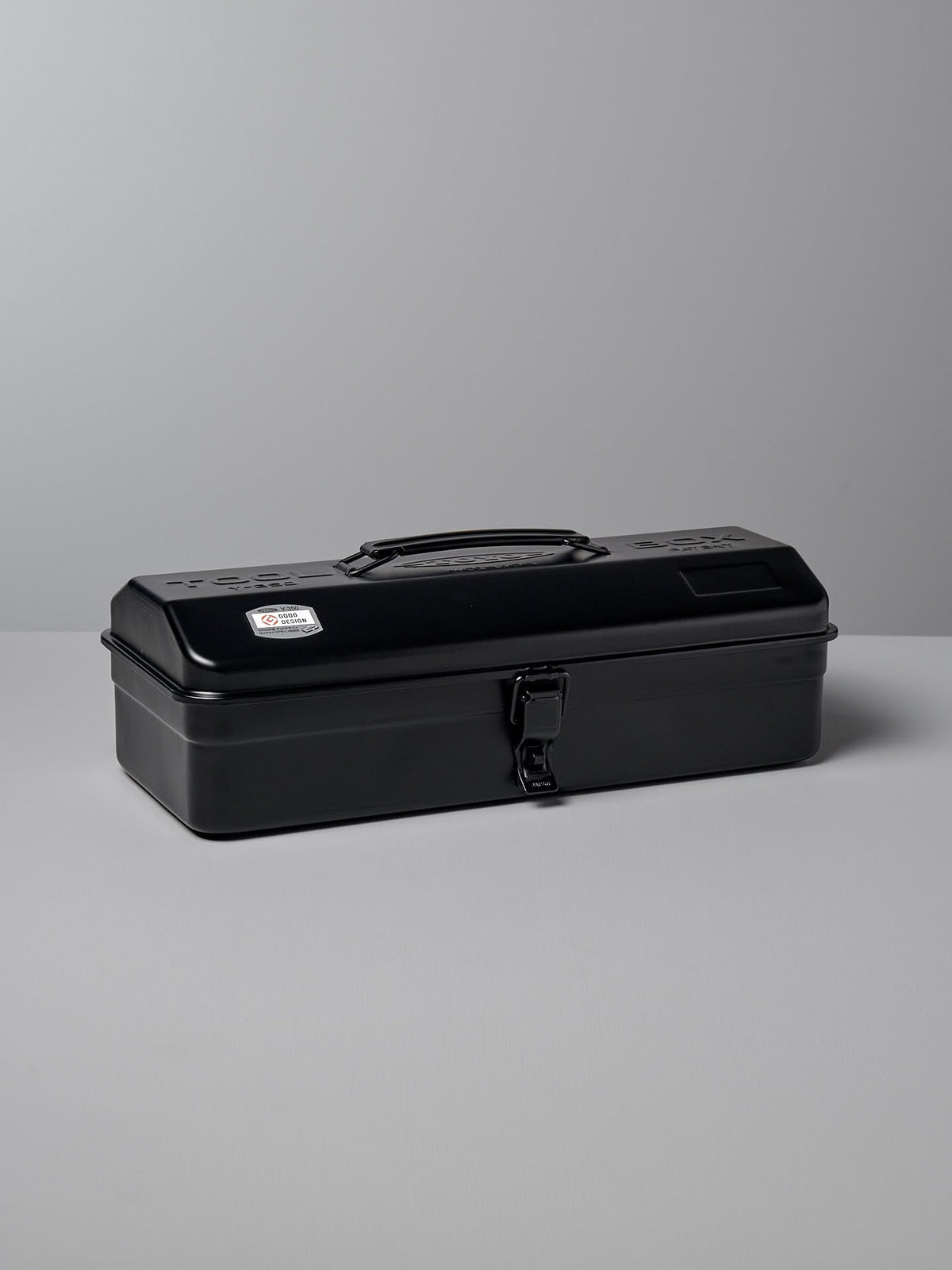 A closed black, camber-top toolbox made from powder-coated steel, featuring a handle on the lid and a latch on the front. This sleek design earned the Camber-Top Toolbox Y-350 – Black by TOYO STEEL the Good Design Award 2009.