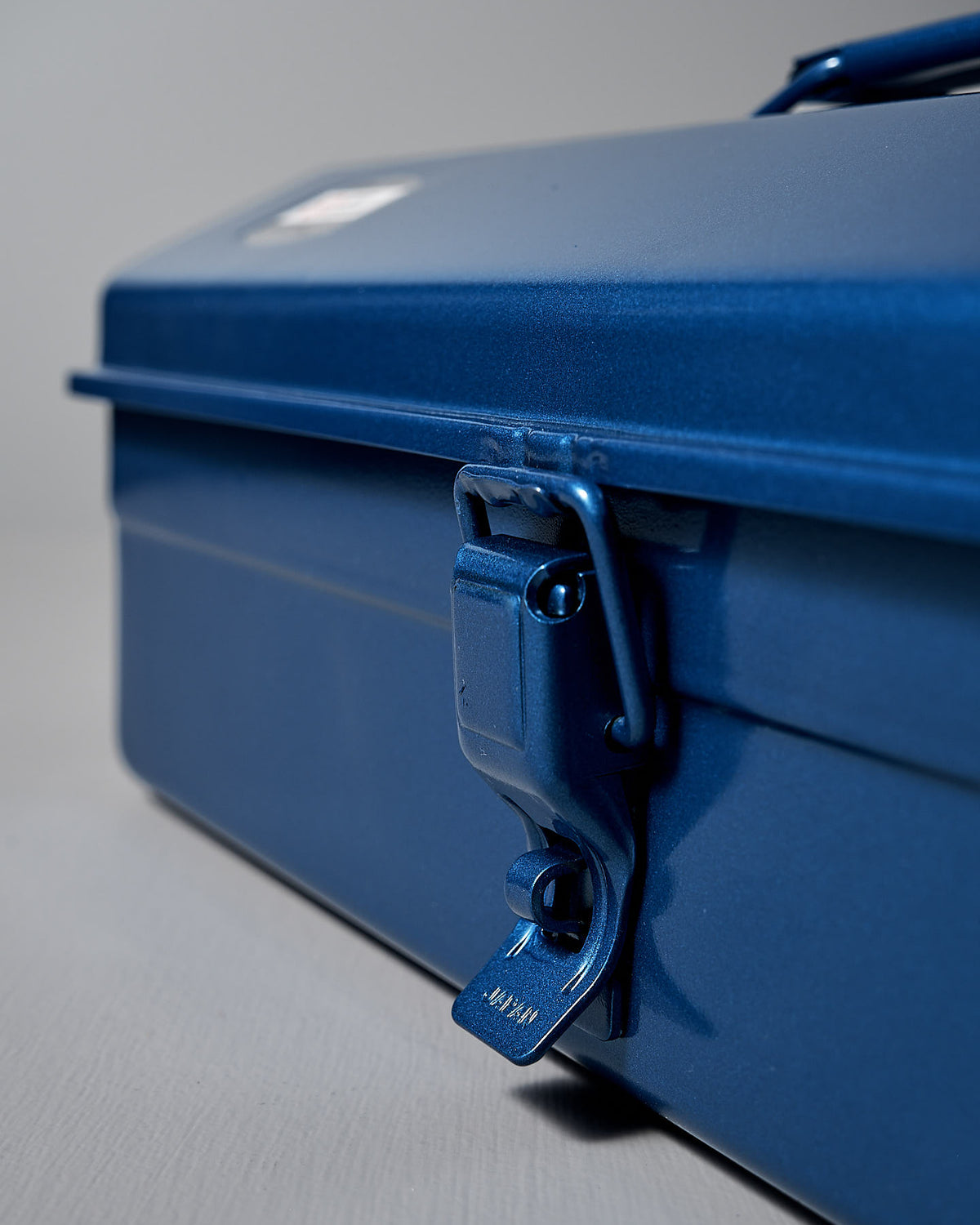Close-up of the TOYO STEEL Camber-Top Toolbox Y-350 in powder-coated blue, a Good Design Award 2009 winner, featuring a secure latch against a gray background.