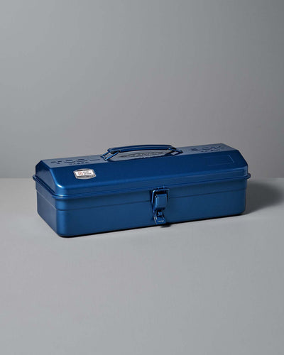 The TOYO STEEL Camber-Top Toolbox Y-350 in blue, featuring a powder-coated steel finish and a sturdy handle with a latch, is elegantly showcased on a gray surface.