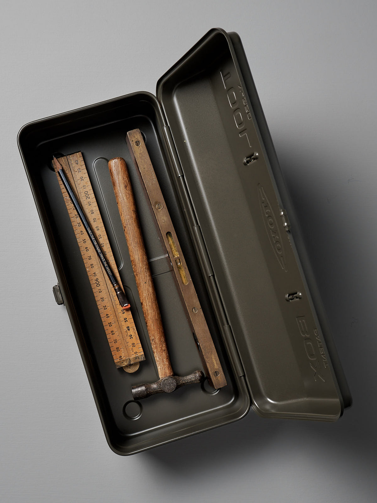 The TOYO STEEL Camber-Top Toolbox Y-350 in Moss Green, crafted from powder-coated steel, comes with a neatly arranged wooden ruler, pencil, wooden level, and small hammer inside.