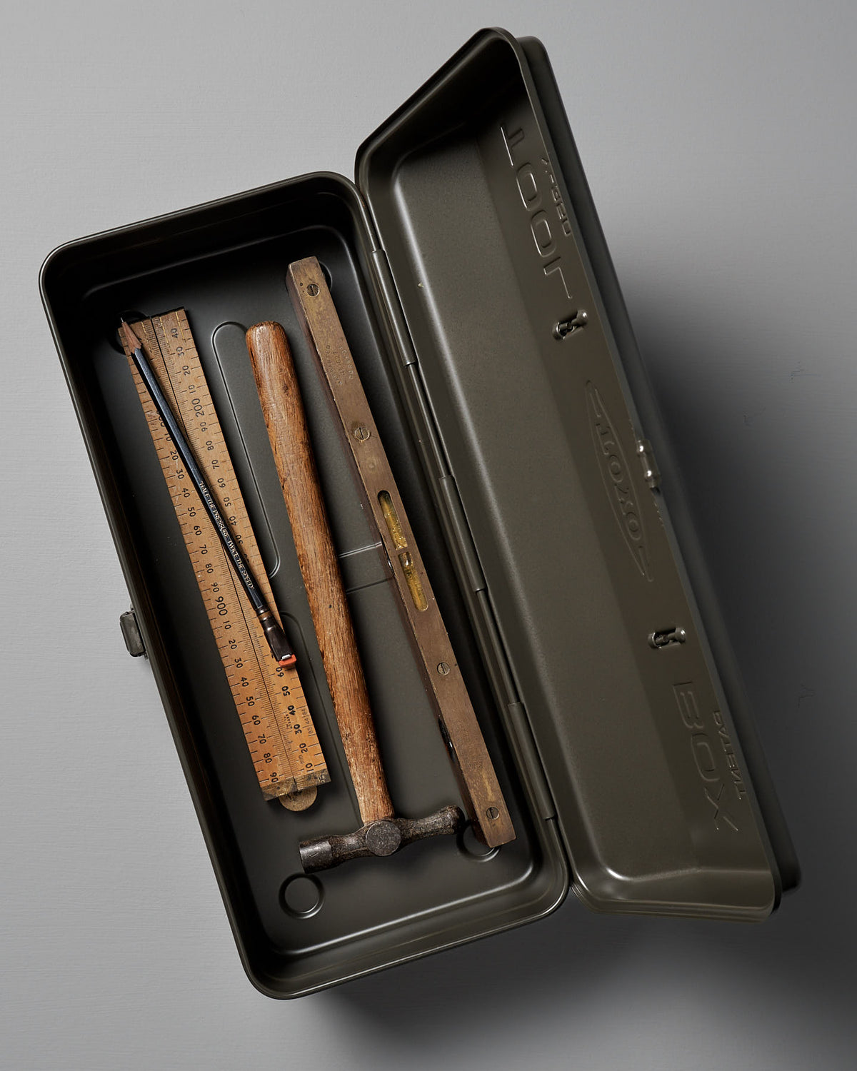The TOYO STEEL Camber-Top Toolbox Y-350 in Moss Green, crafted from powder-coated steel, comes with a neatly arranged wooden ruler, pencil, wooden level, and small hammer inside.