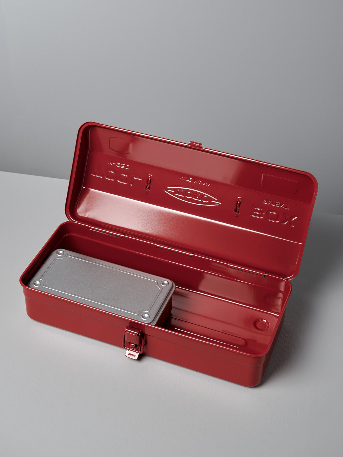 Open Camber-Top Toolbox Y-350 – Red with a grey metal container inside, placed on a grey surface. This meticulously crafted toolbox by TOYO STEEL, boasts robust steel construction for lasting durability and style.