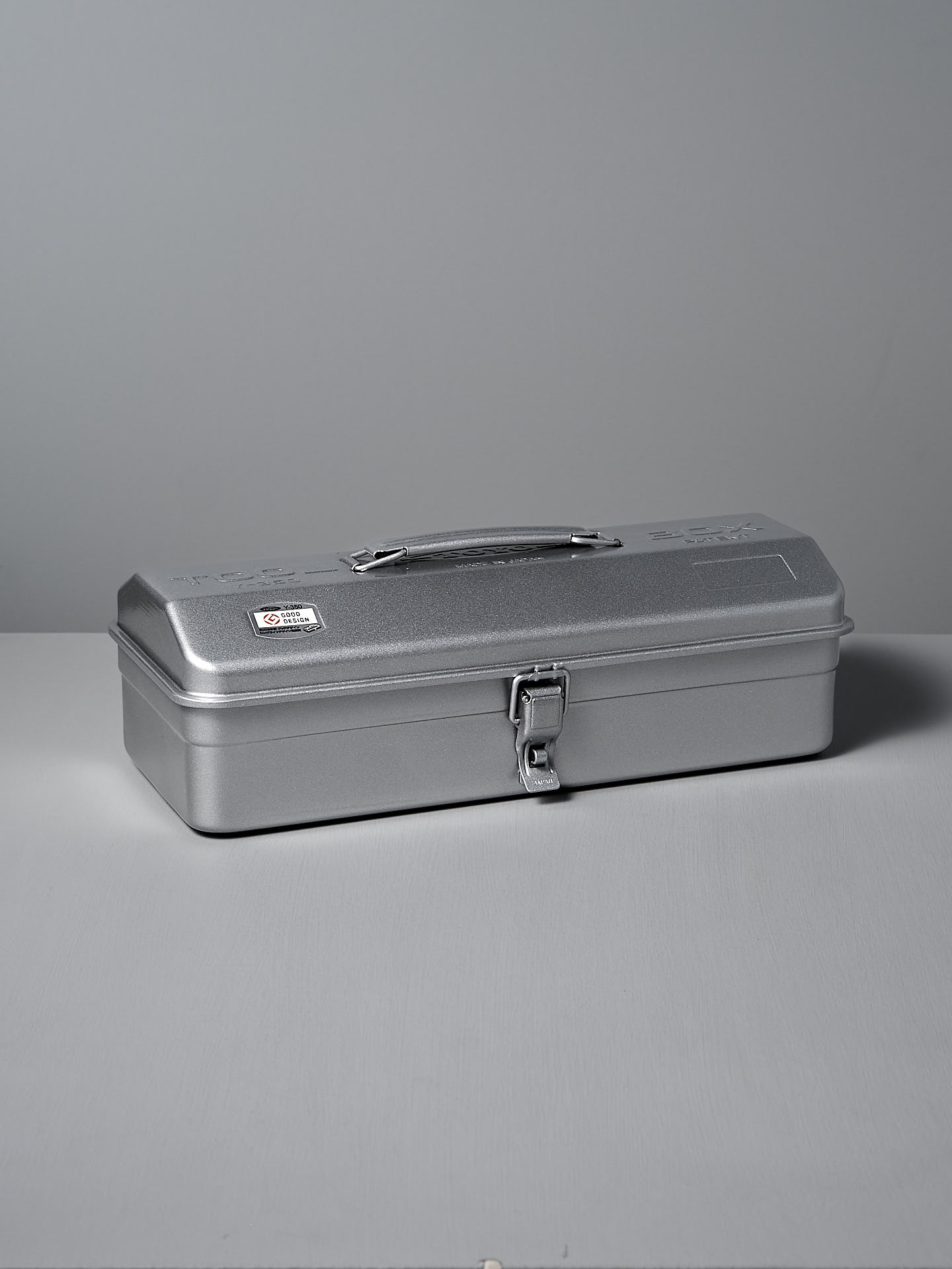 The TOYO STEEL Camber-Top Toolbox Y-350 in powder-coated silver elegantly rests on a gray surface, blending with the matching background.