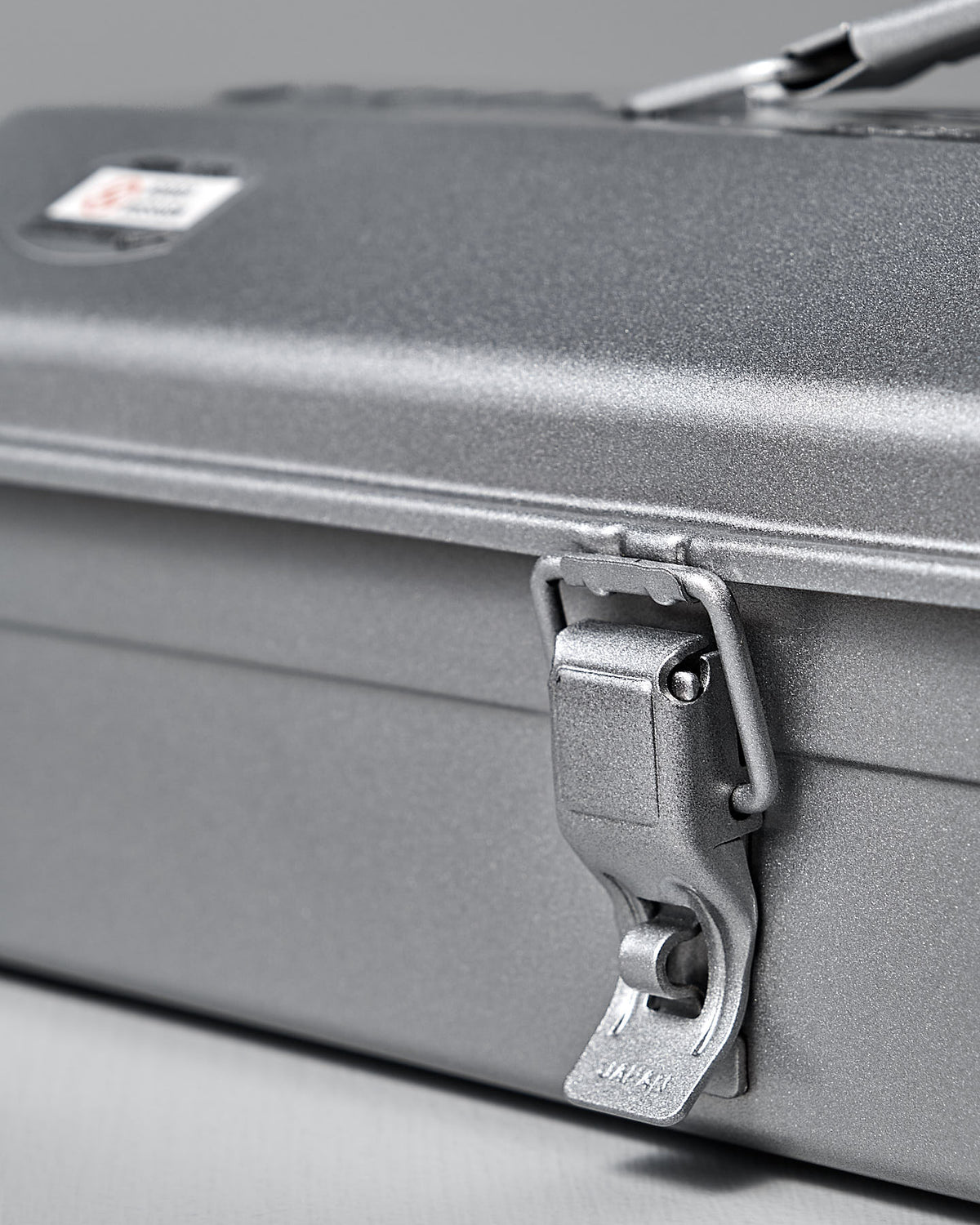 A close-up of the Camber-Top Toolbox Y-350 by TOYO STEEL shows off its sleek, closed design with a latch. The durable, powder-coated steel label is visible in the top corner.