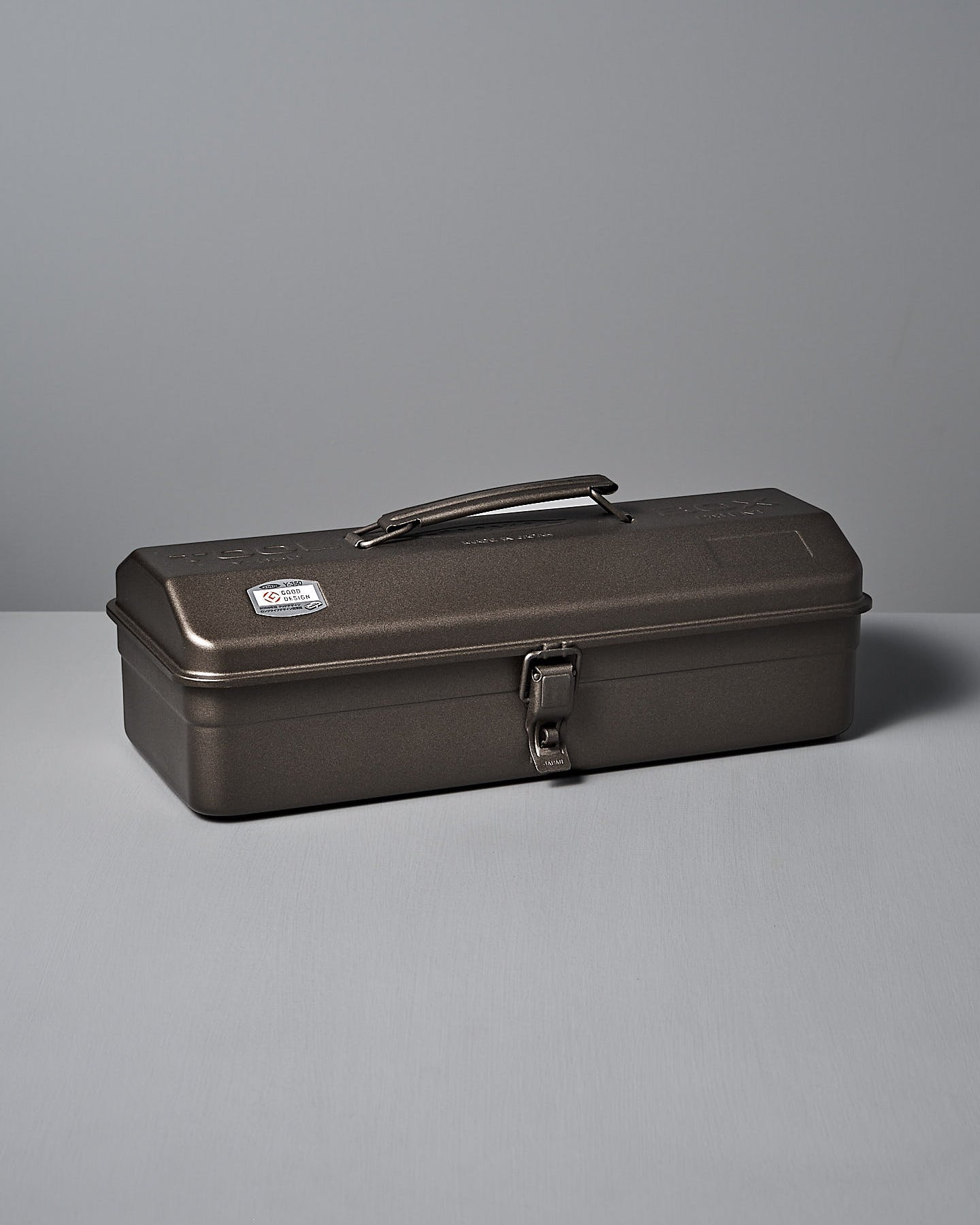 The TOYO STEEL Camber-Top Toolbox Y-350 – Titanium, made from powder-coated steel with a secure latch and sturdy handle, elegantly rests on a flat surface against a plain backdrop, embodying the Good Design Award 2009 standards.