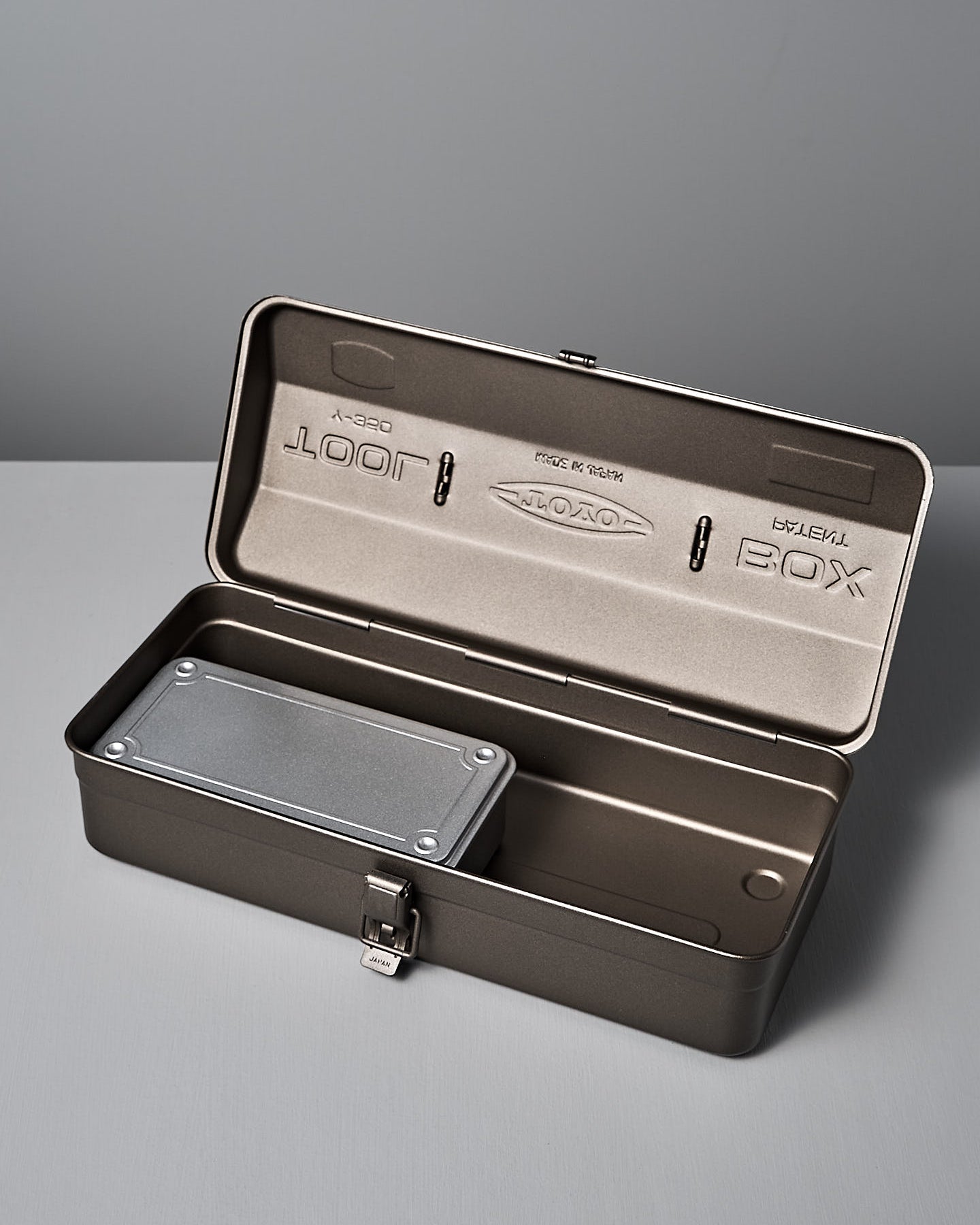 The TOYO STEEL Camber-Top Toolbox Y-350 – Titanium, made from powder-coated steel with a secure latch and sturdy handle, elegantly rests on a flat surface against a plain backdrop, embodying the Good Design Award 2009 standards.