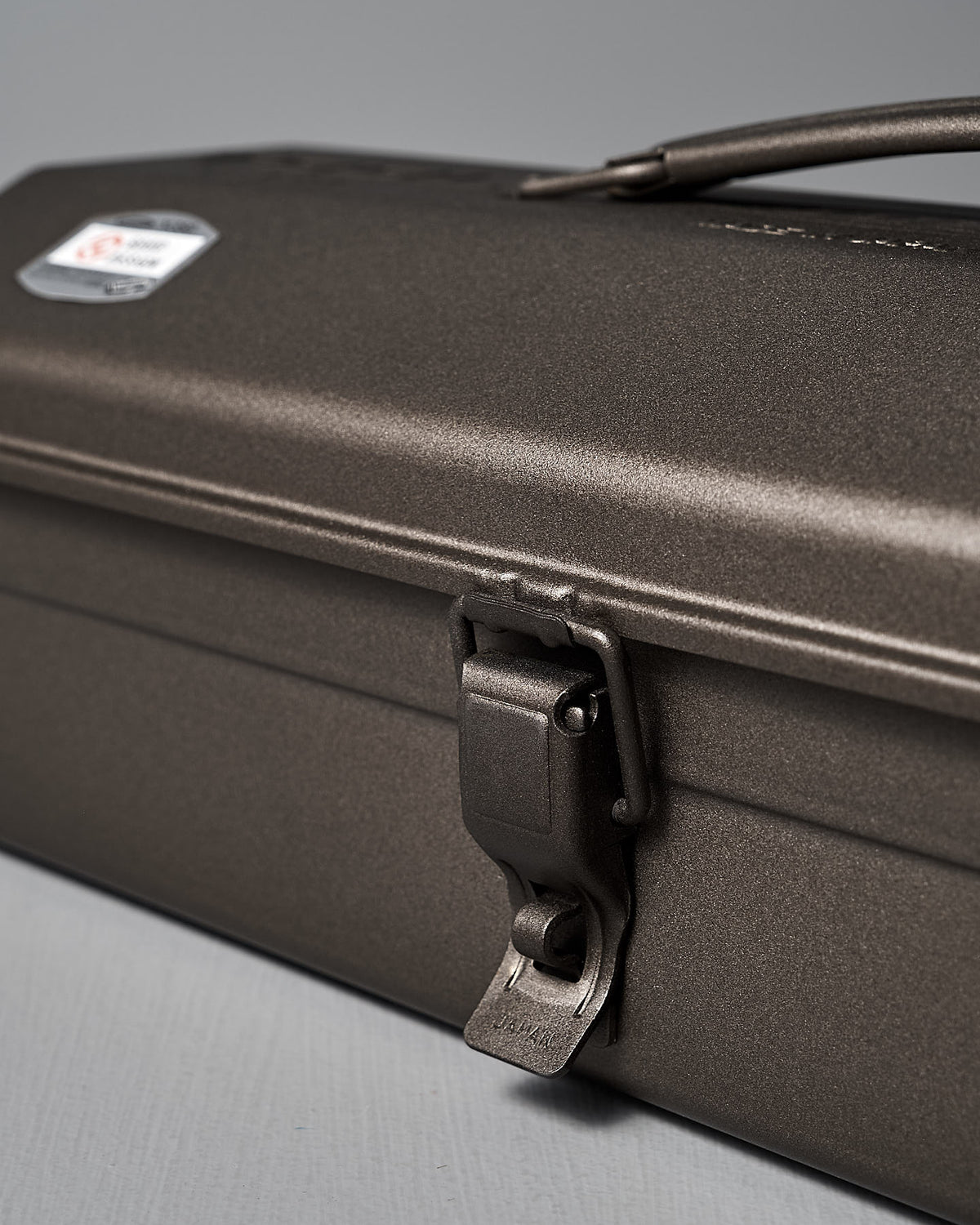 A close-up of the TOYO STEEL Camber-Top Toolbox Y-350 in titanium, crafted from powder-coated steel. It features a latch, handle, and textured finish with one visible logo on top, embodying its Good Design Award 2009 recognition.