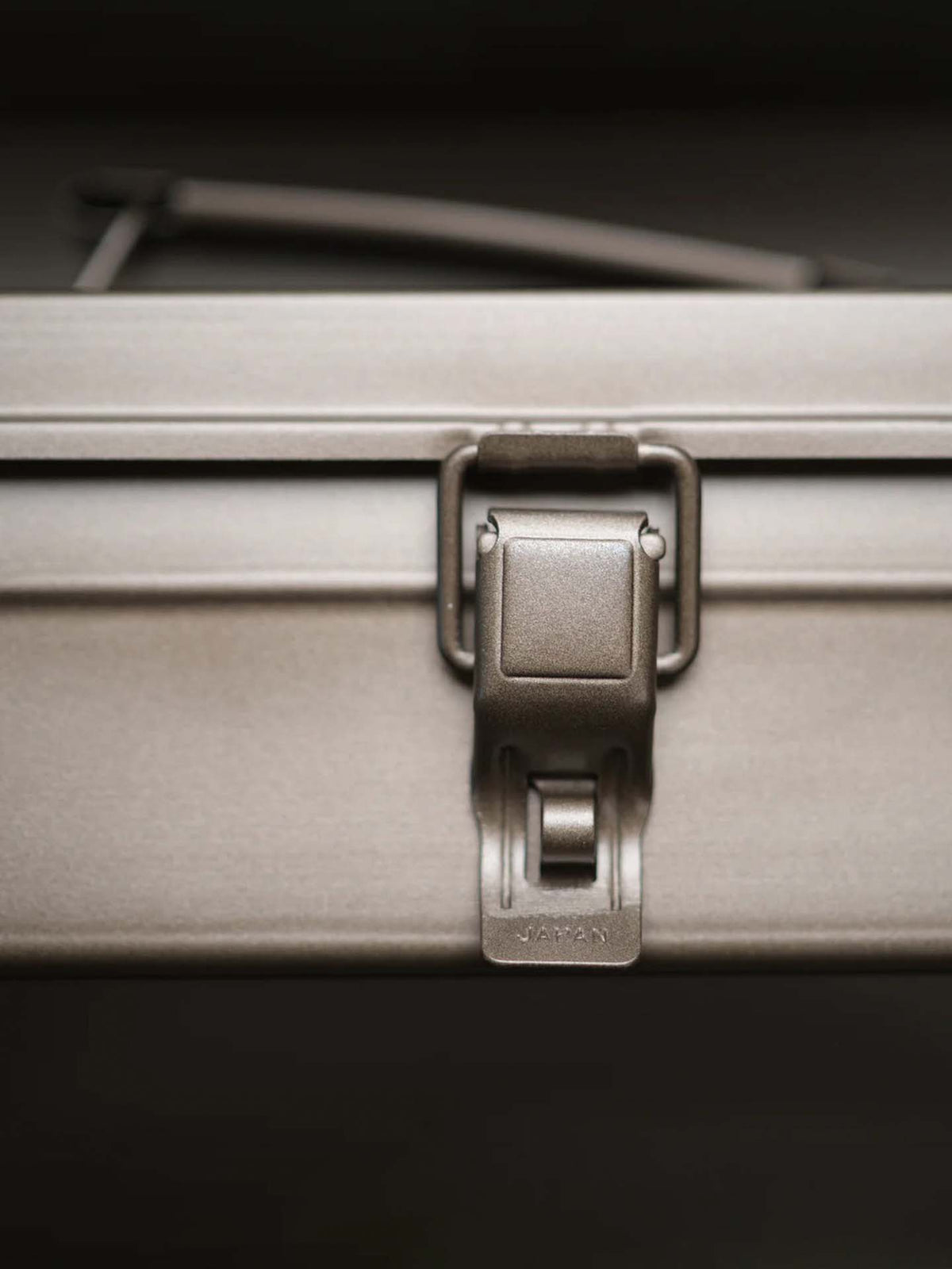 A close-up of a metal latch on the Camber-Top Toolbox Y-350 – Titanium by TOYO STEEL, showcasing &quot;JAPAN&quot; engraved on it. This seamless hard-shell design won the Good Design Award in 2009.